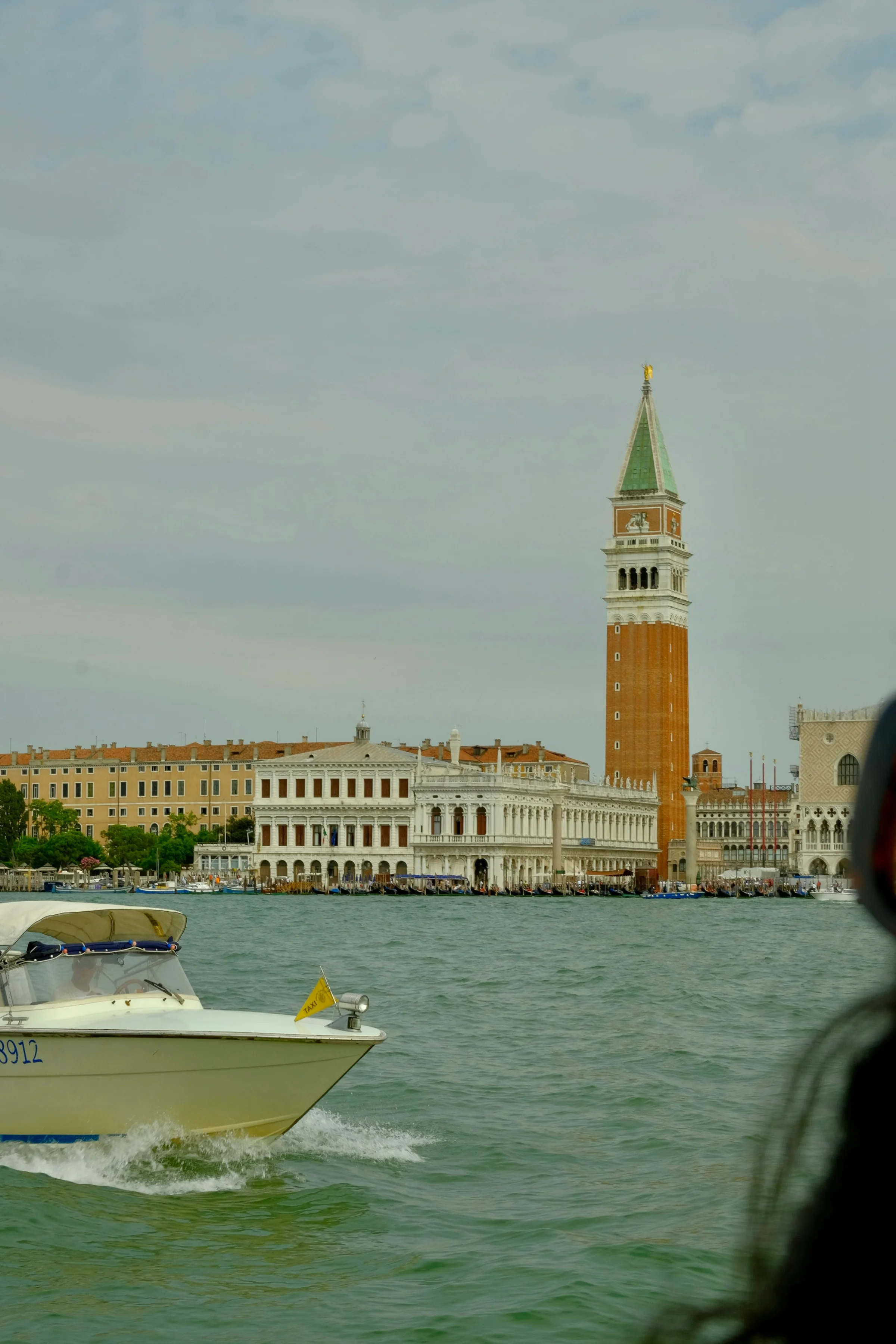 Perahu motor putih di laguna Venice dengan menara Campanile San Marco di kejauhan.