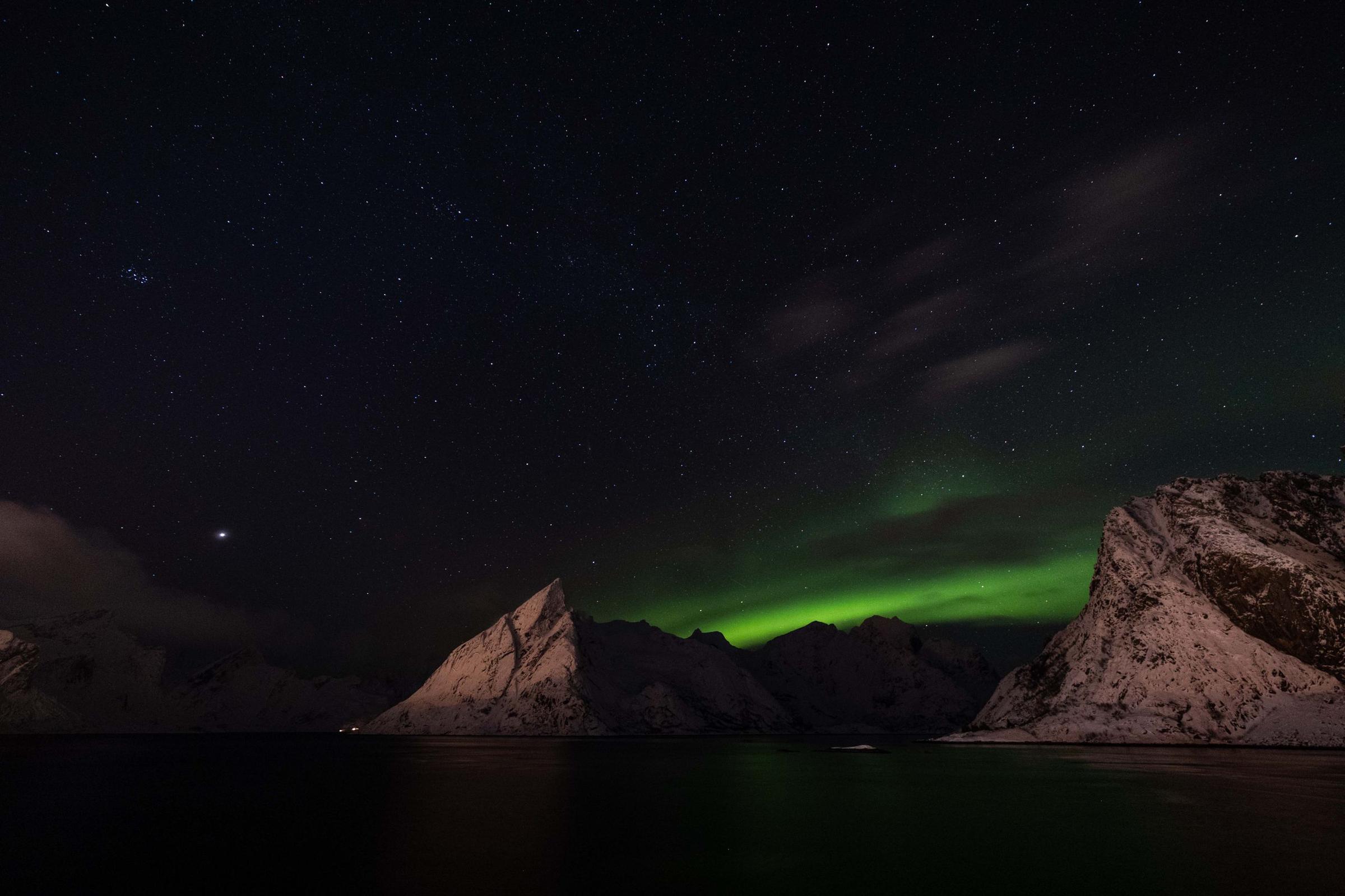 Aurora hijau di atas pegunungan Lofoten yang bersalju, Norwegia.