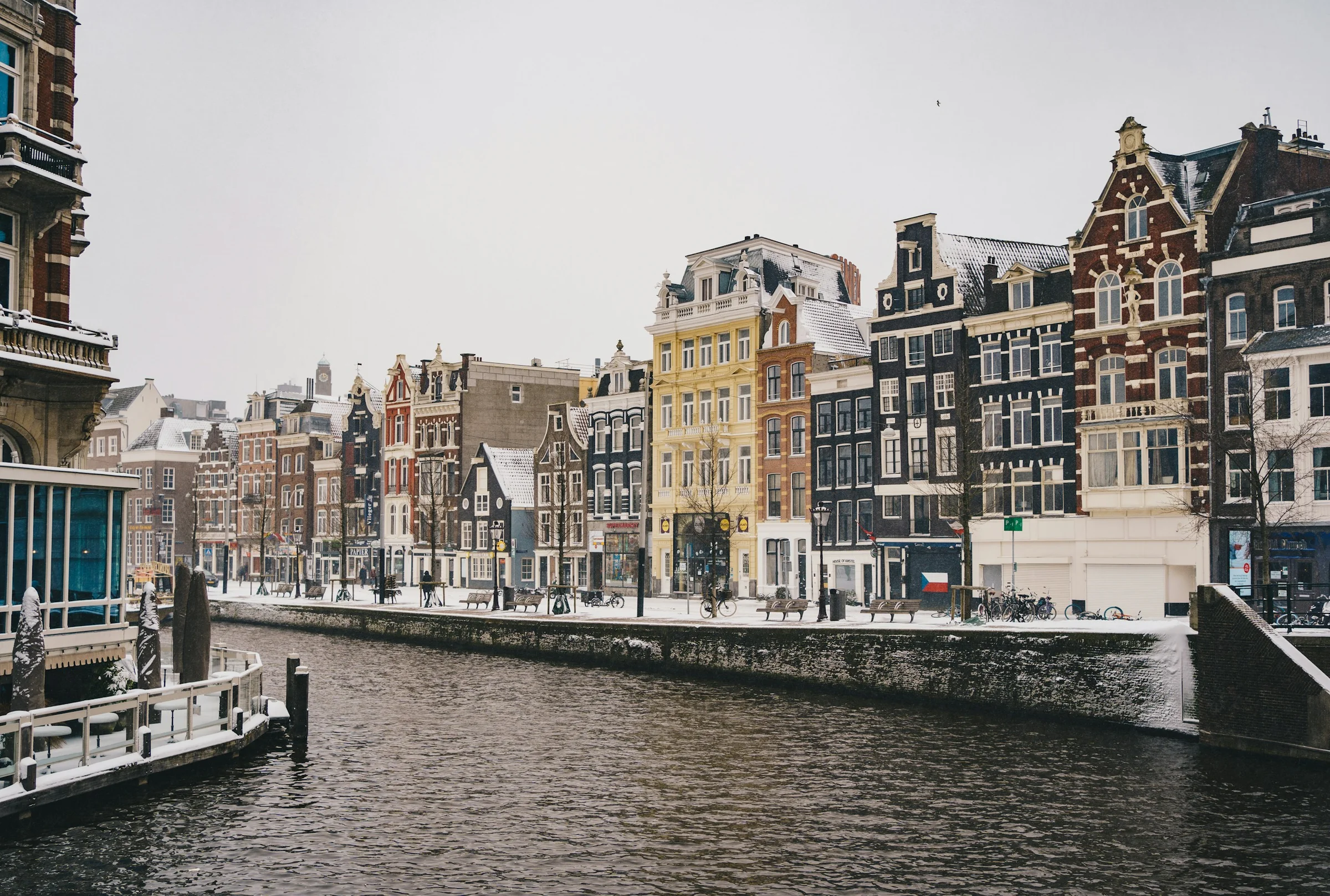 Rumah-rumah kanal Amsterdam dengan sisa salju di tepi kanal pada hari kelabu.