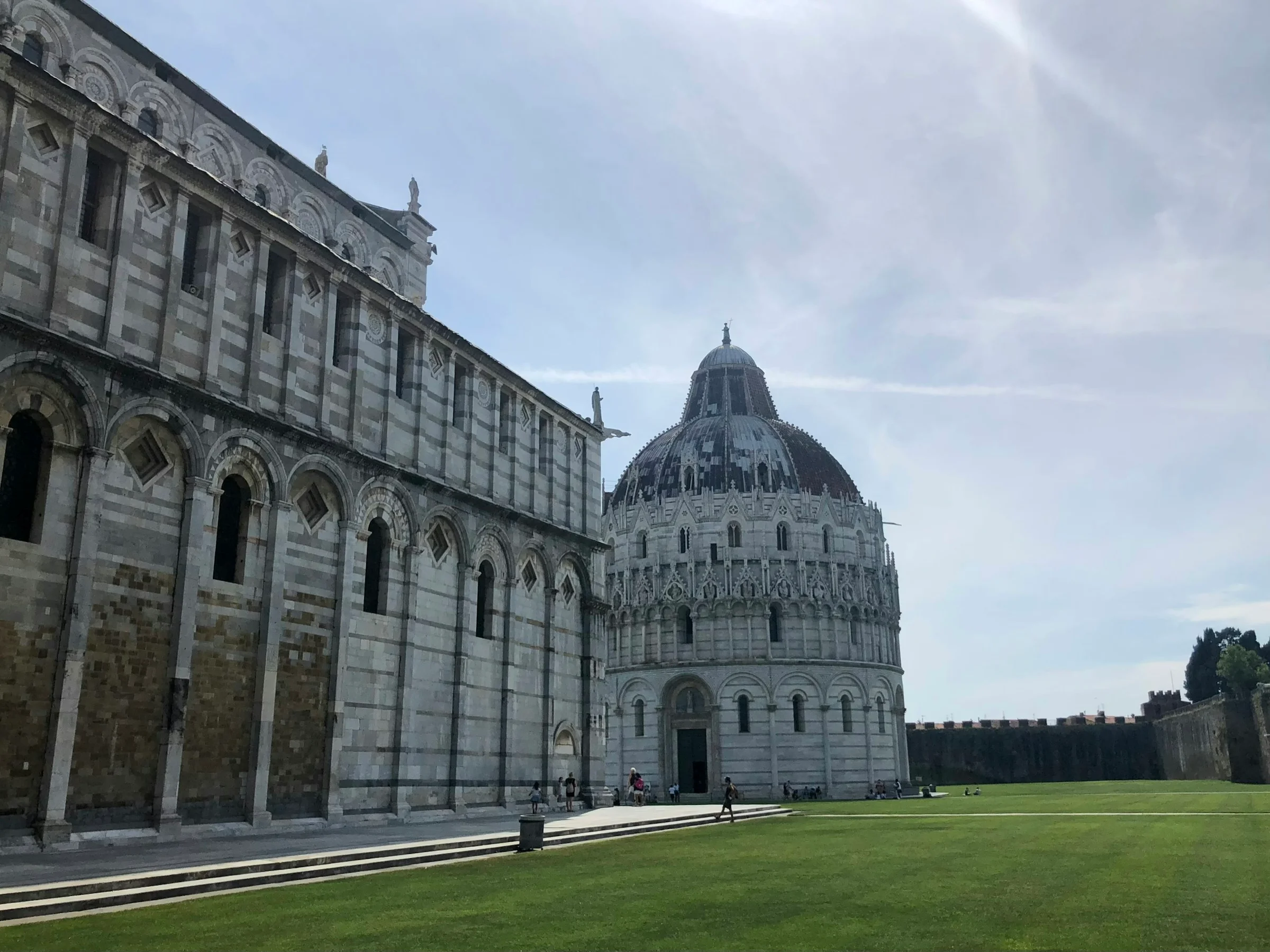 Baptistery dan sisi Katedral Pisa di bawah langit berawan lembut.