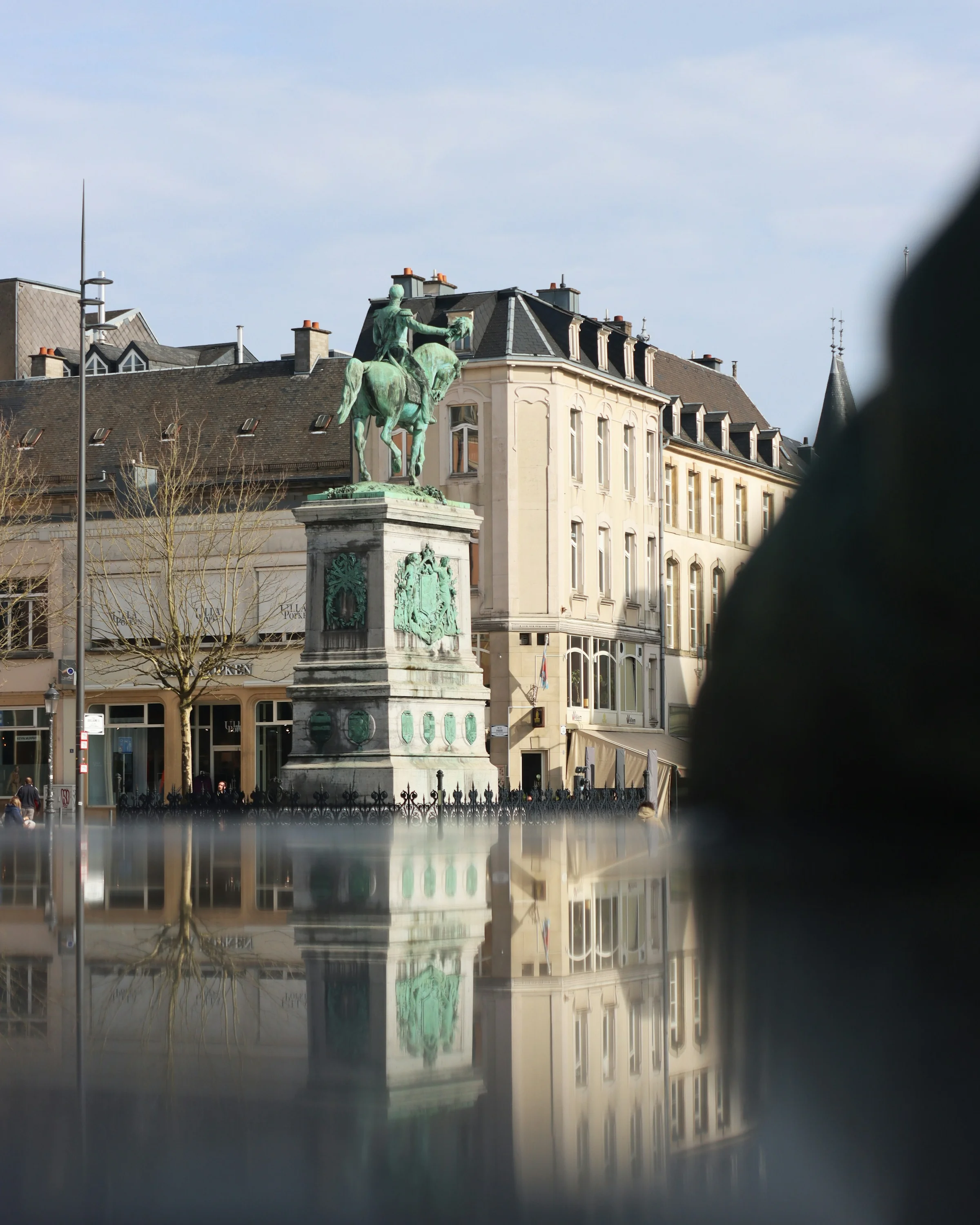 Patung berkuda Place Guillaume II di Luxembourg dengan pantulannya di permukaan basah.