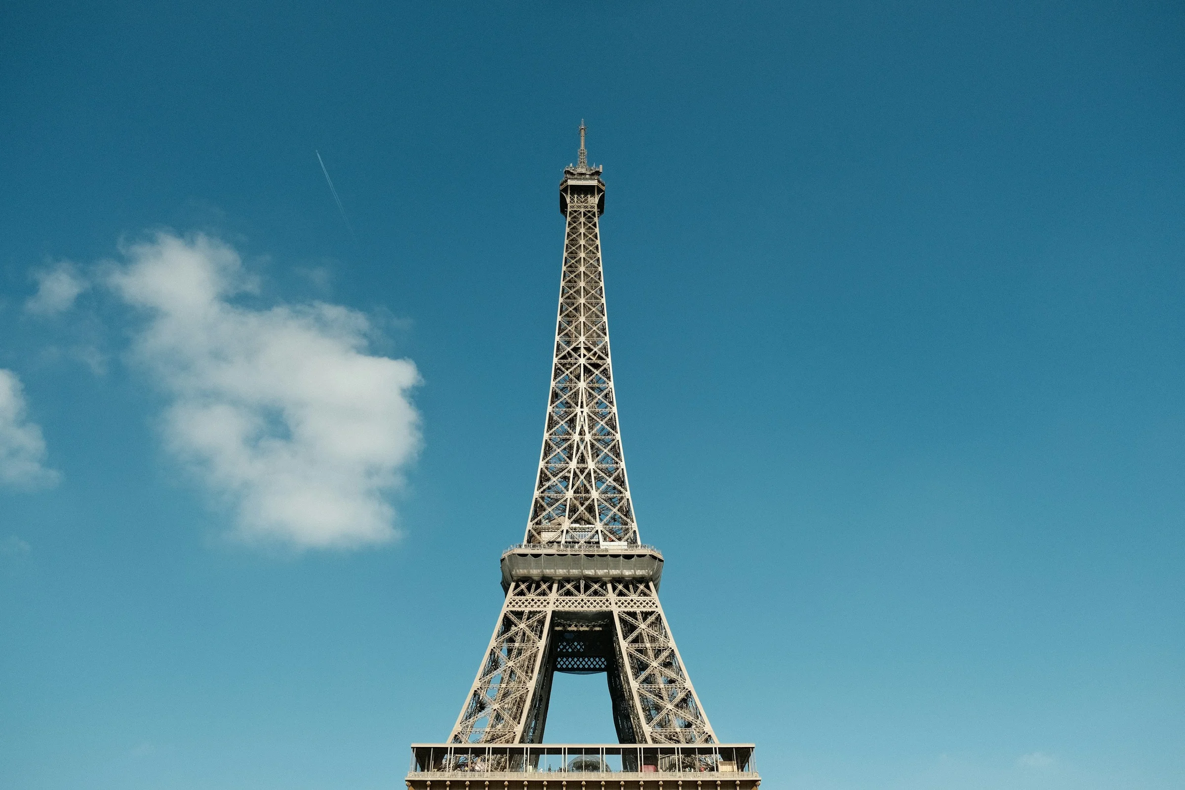 Menara Eiffel di Paris dengan langit biru jernih dan awan putih tipis.