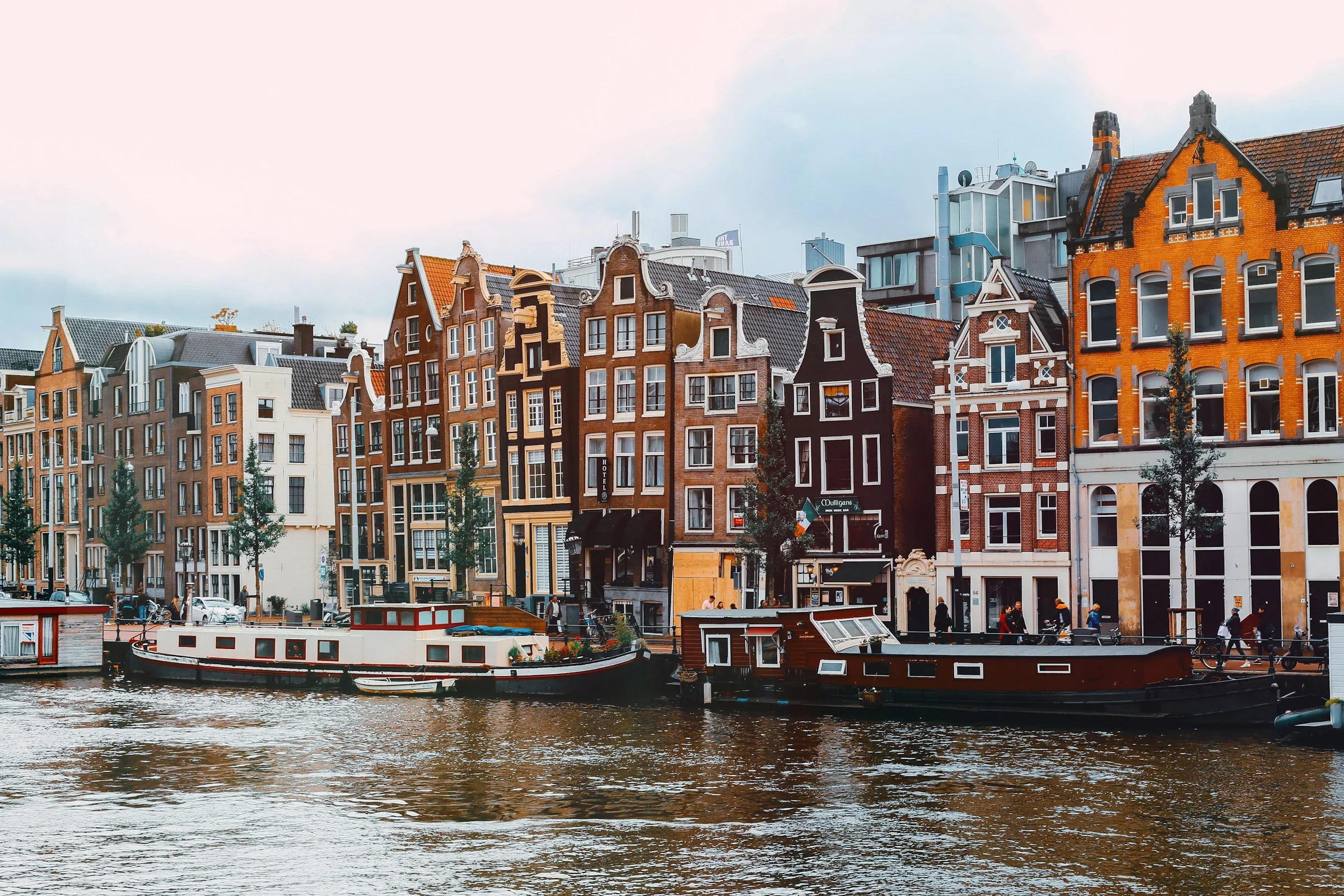 Rumah-rumah kanal Amsterdam dengan perahu tertambat di bawah langit berawan.