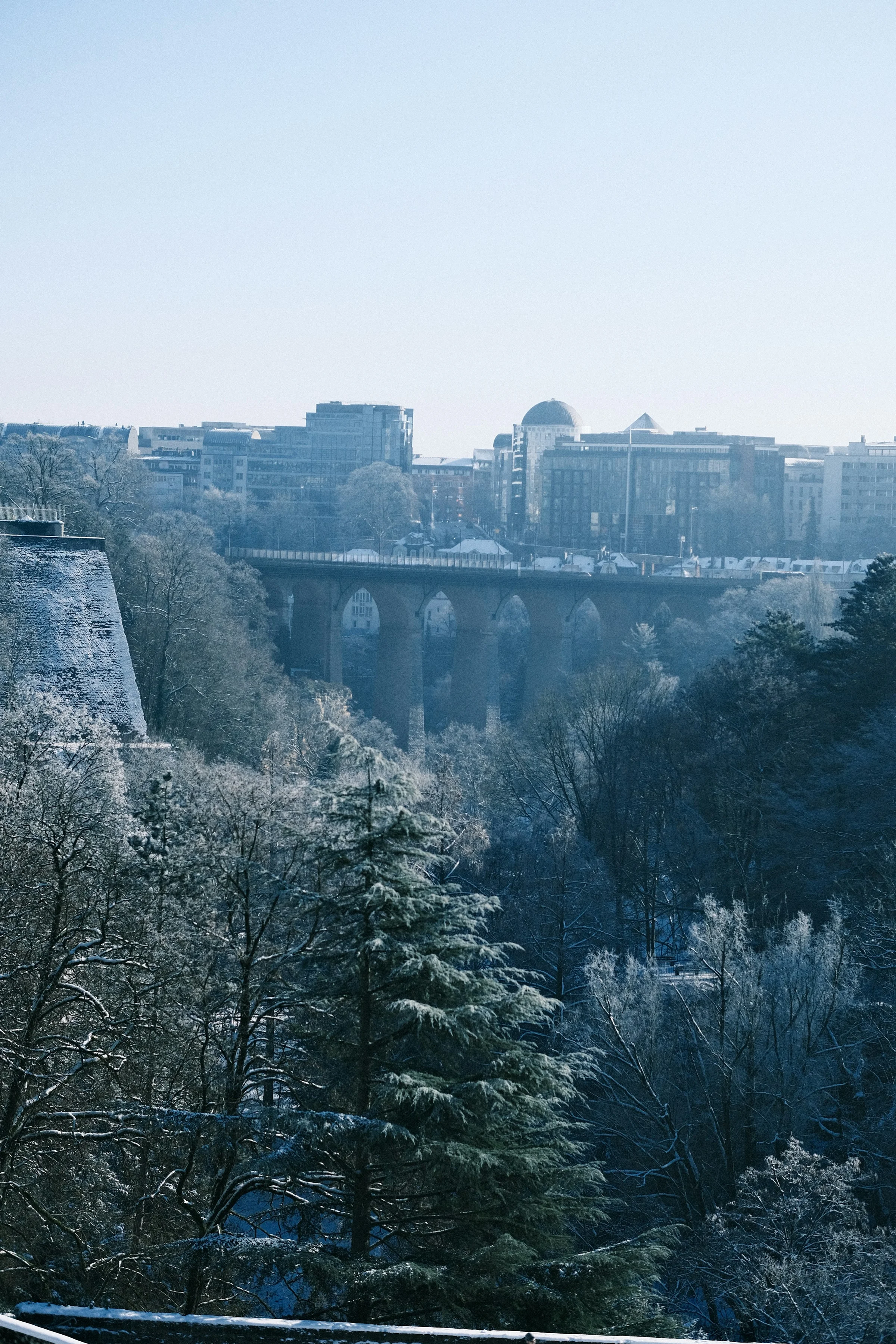 Jembatan batu di atas ngarai berhutan dengan pepohonan berselimut embun beku di Luxembourg.