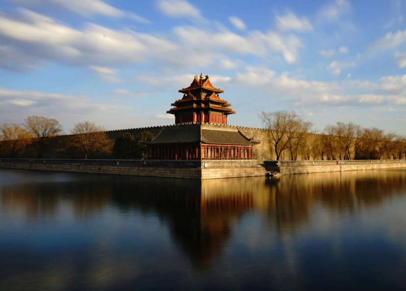 Menara sudut Kota Terlarang Beijing dengan refleksi di parit, cahaya keemasan.