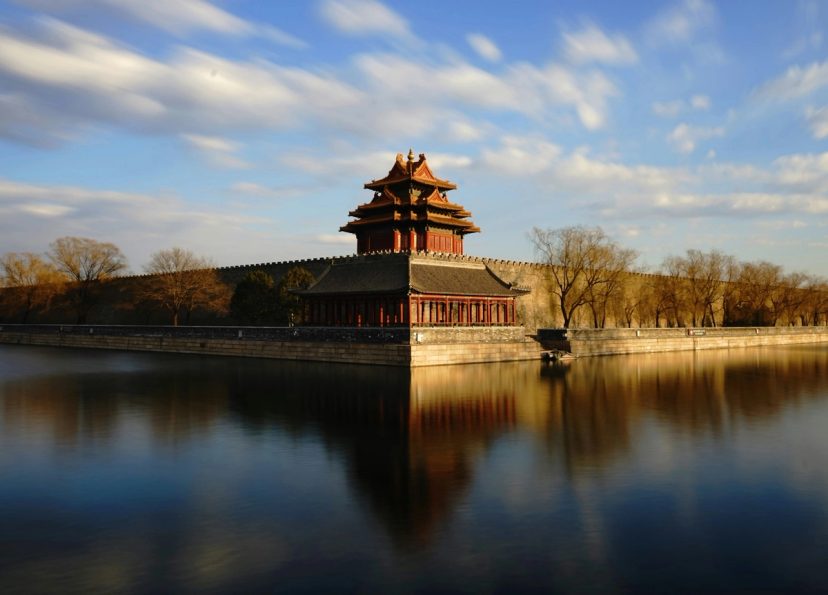 Menara sudut Kota Terlarang Beijing dengan refleksi di parit, cahaya keemasan.