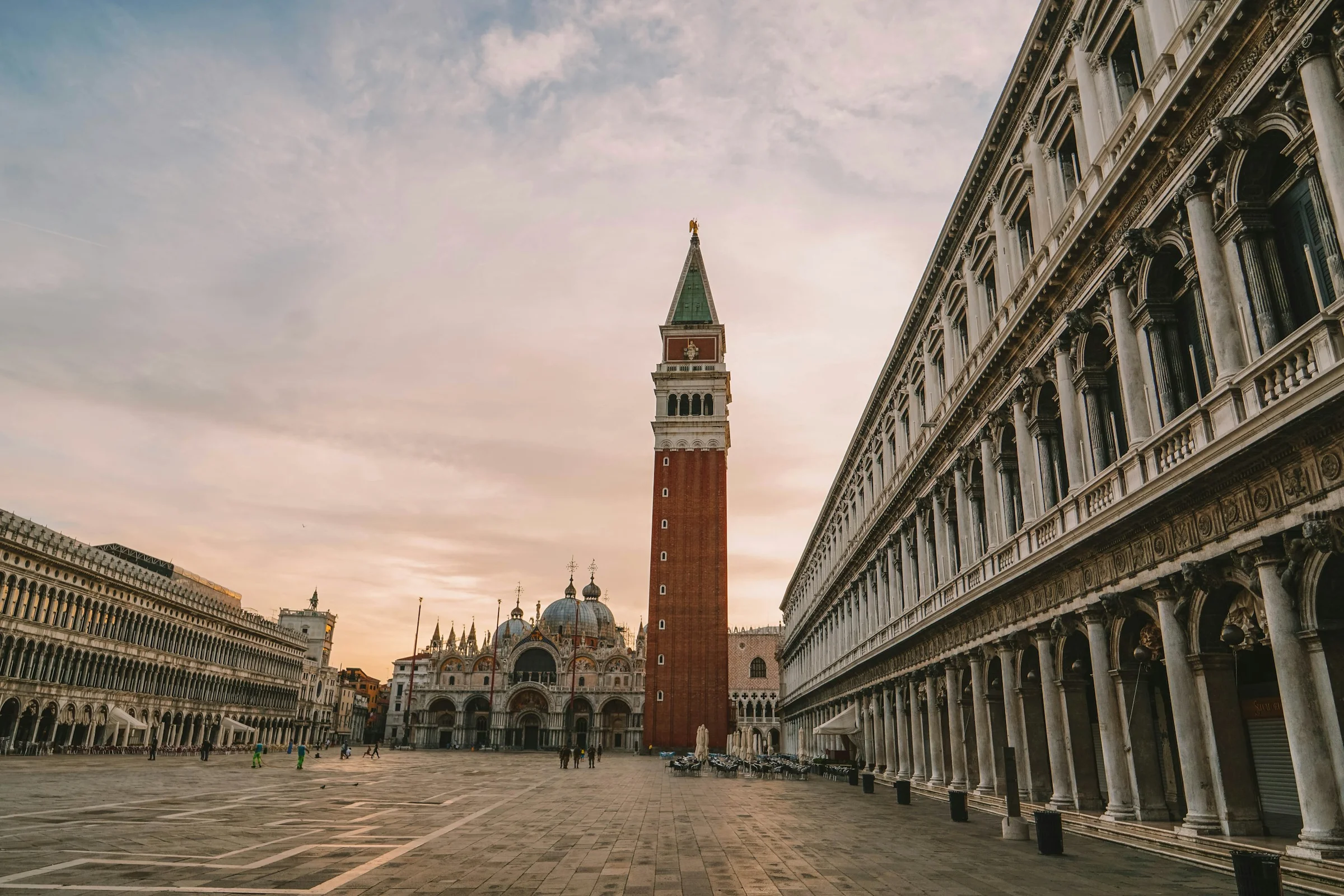 Basilika dan lengkung arkade Piazza San Marco di Venice yang lengang, langit hangat berawan.