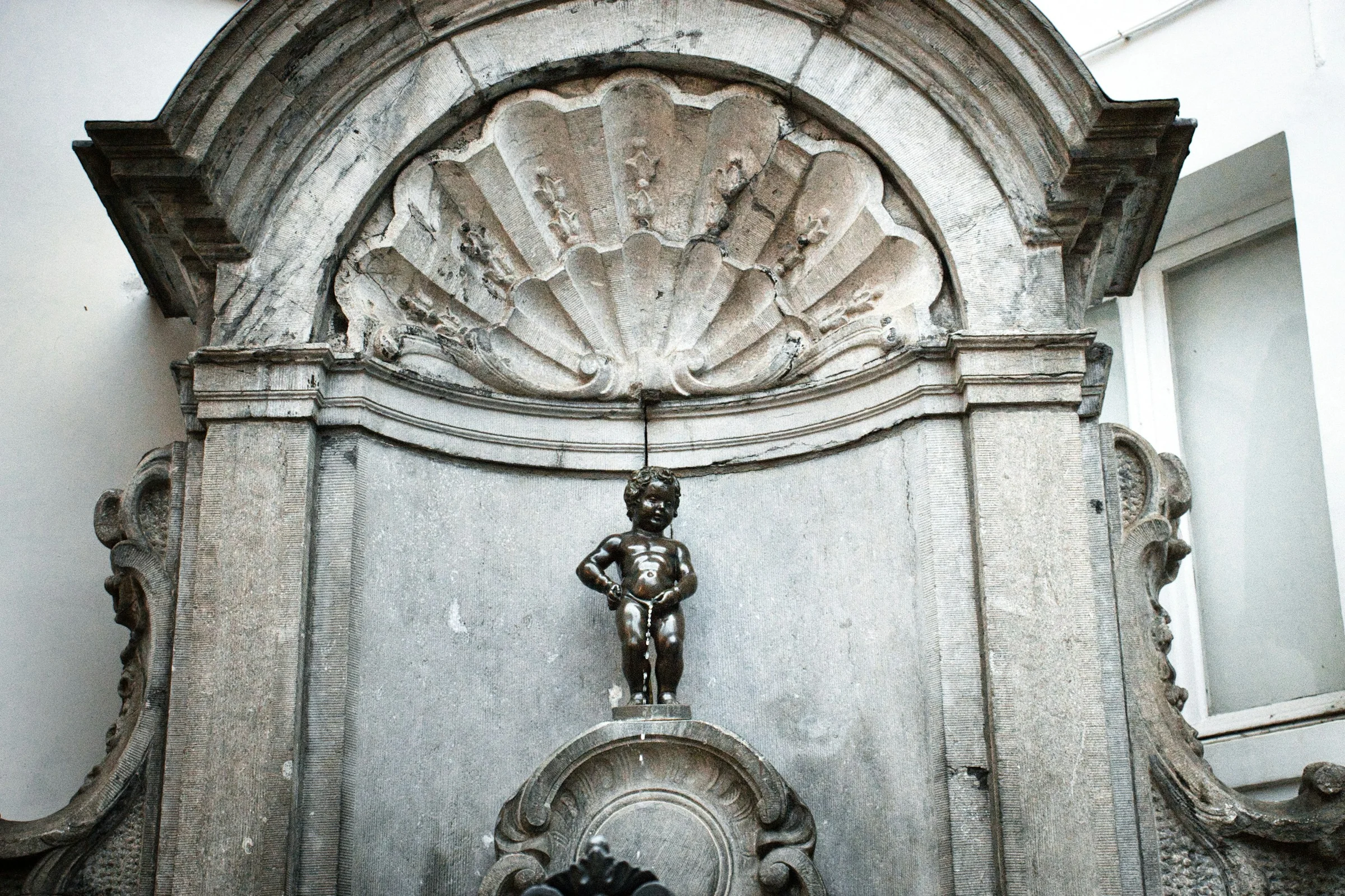 Patung Manneken Pis di Brussels di dalam relung bercorak kerang.