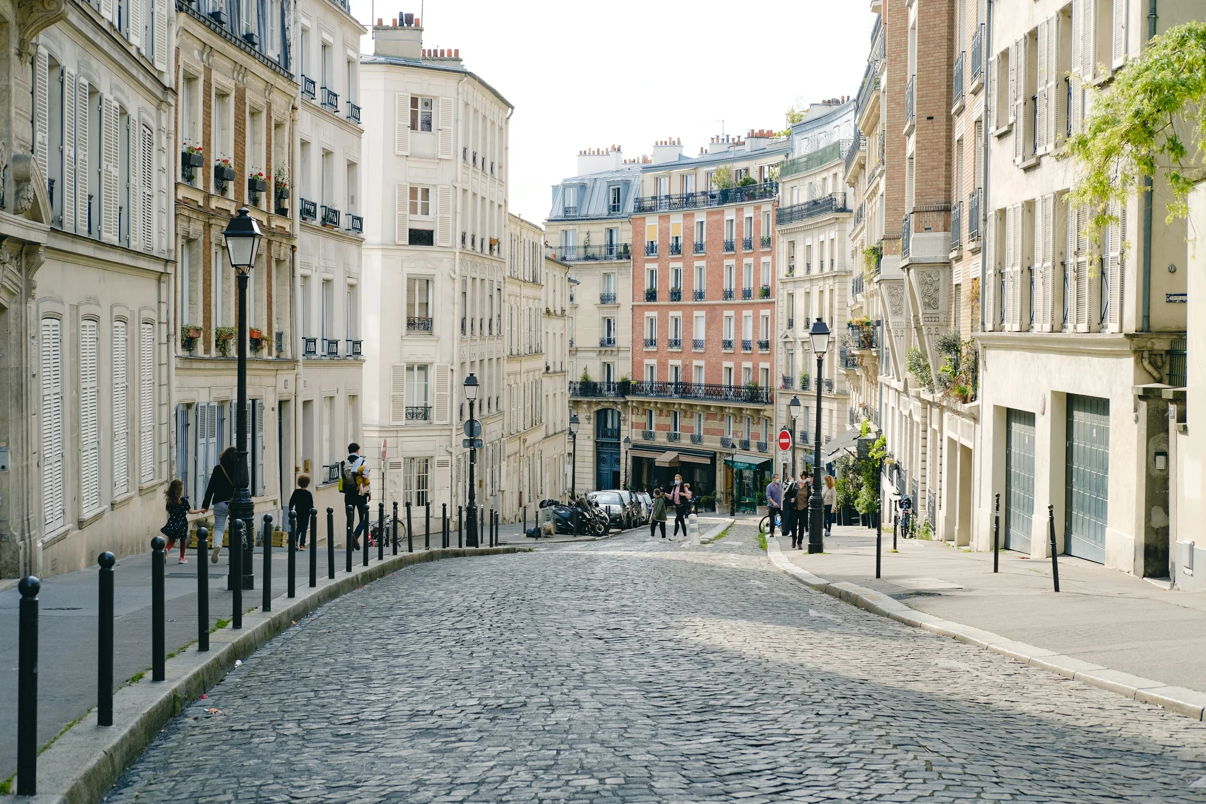 Jalan berbatu yang lengang di Paris pagi hari dengan deretan bangunan krem dan pohon gundul.
