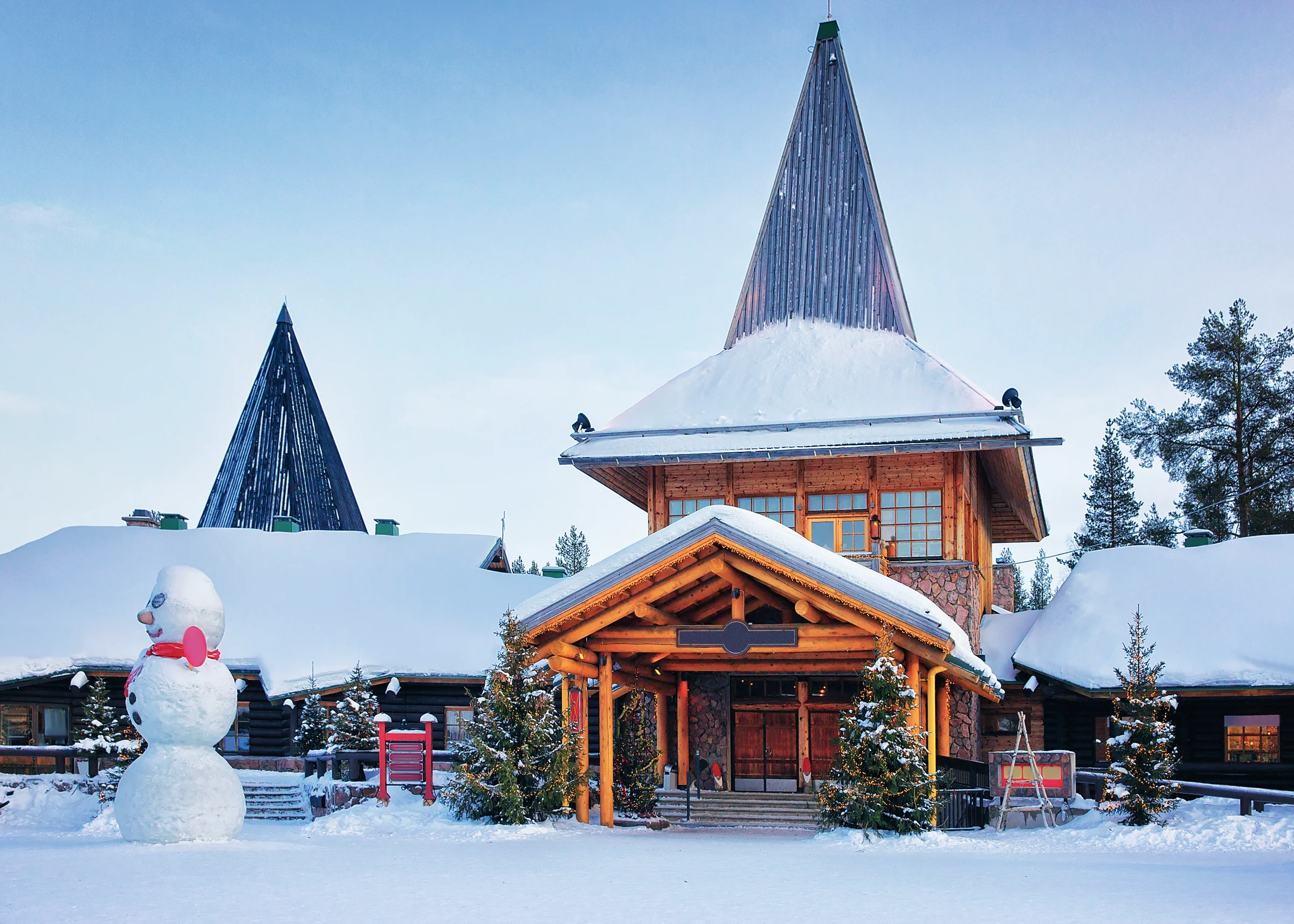 Pondok kayu Santa Claus Village di Rovaniemi bersalju dengan manusia salju di halaman
