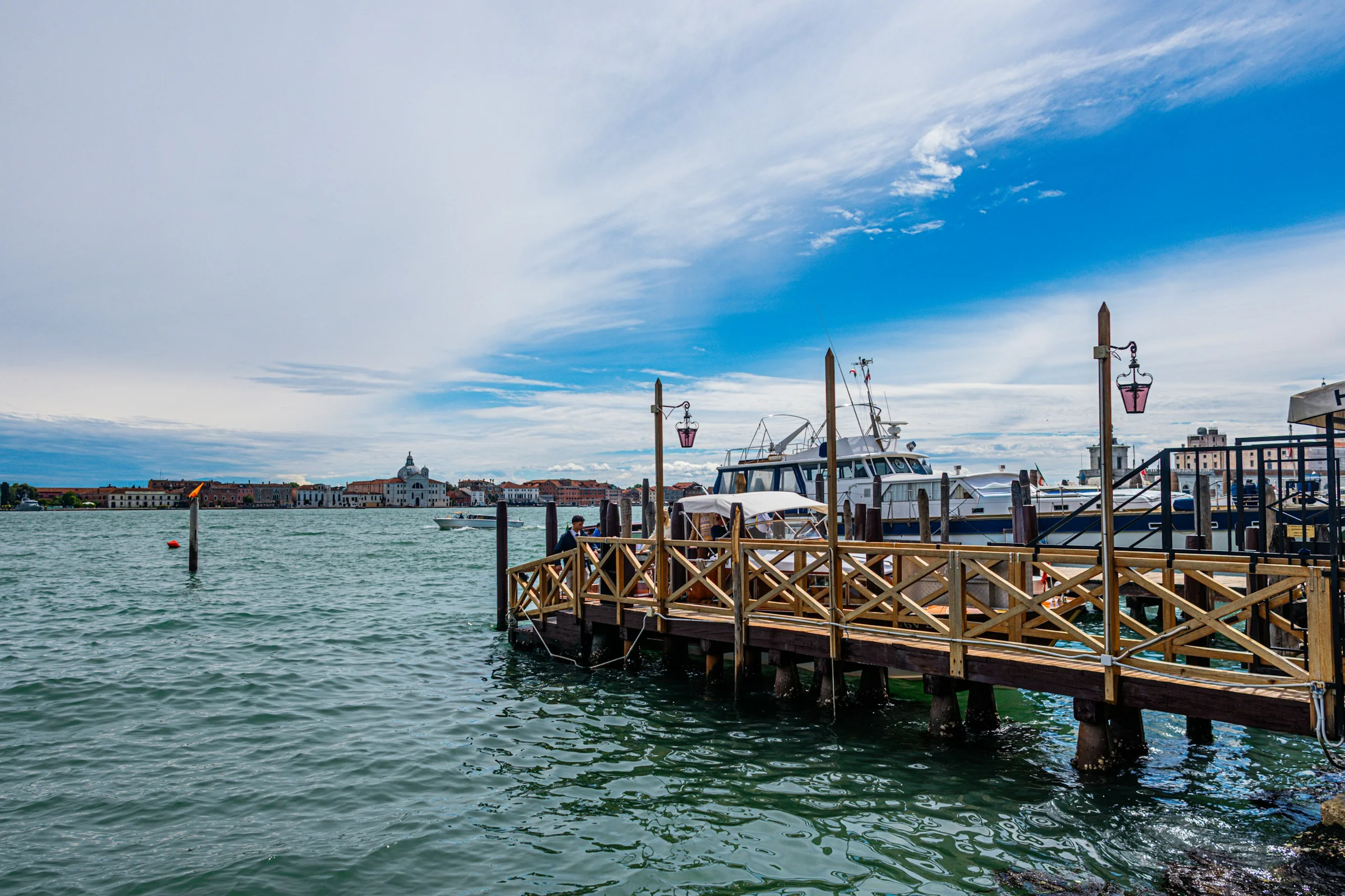 Dermaga kayu di laguna Venice dengan langit biru dan awan tipis.