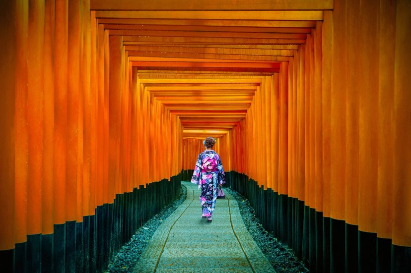 Wisatawan berjaket puffer membawa kamera di tepi Danau Kawaguchi dengan Gunung Fuji dan langit senja jingga