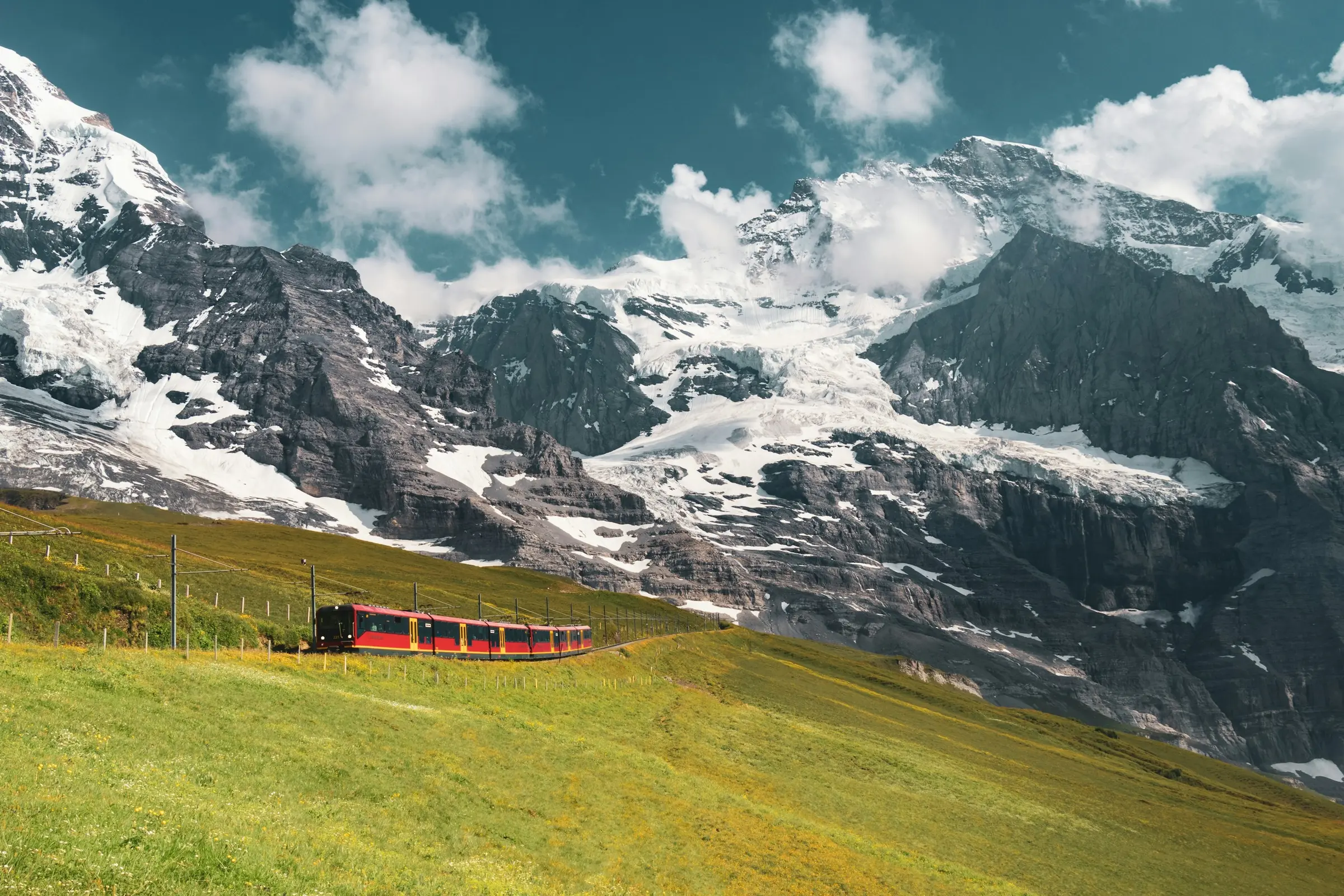 Kereta merah Jungfraubahn melintasi padang rumput pegunungan Alpen bersalju