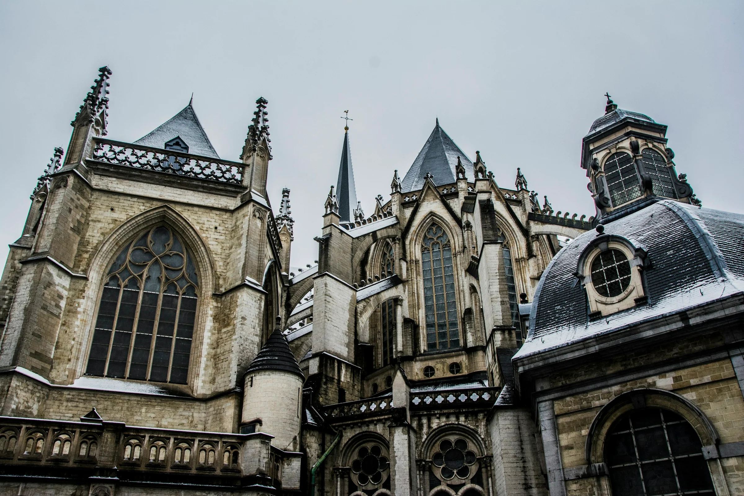 Sisi Katedral Santo Mikael dan Santa Gudula di Brussels dengan salju tipis di atap dan langit mendung.