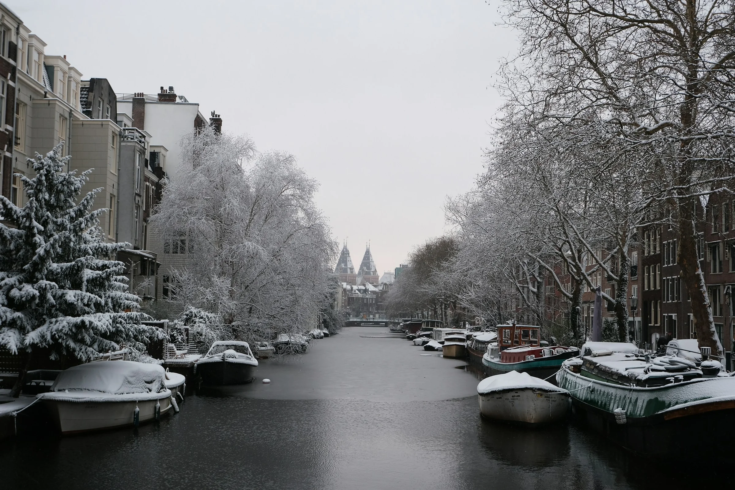 Kanal Amsterdam dengan pohon berselimut salju dan perahu-perahu yang tertutup salju.