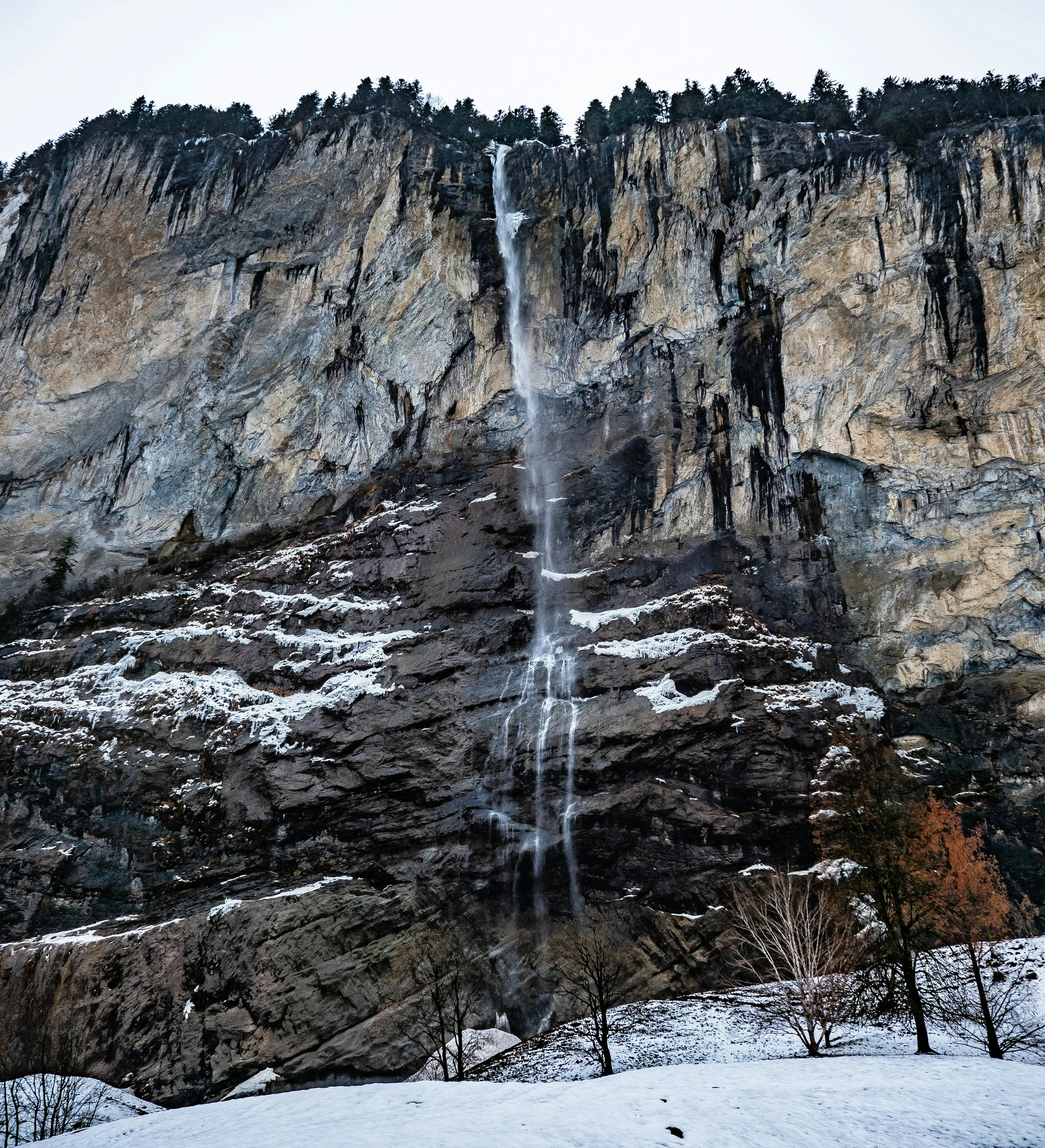 Air terjun Staubbach di tebing Lauterbrunnen dengan sisa salju di kaki tebing.