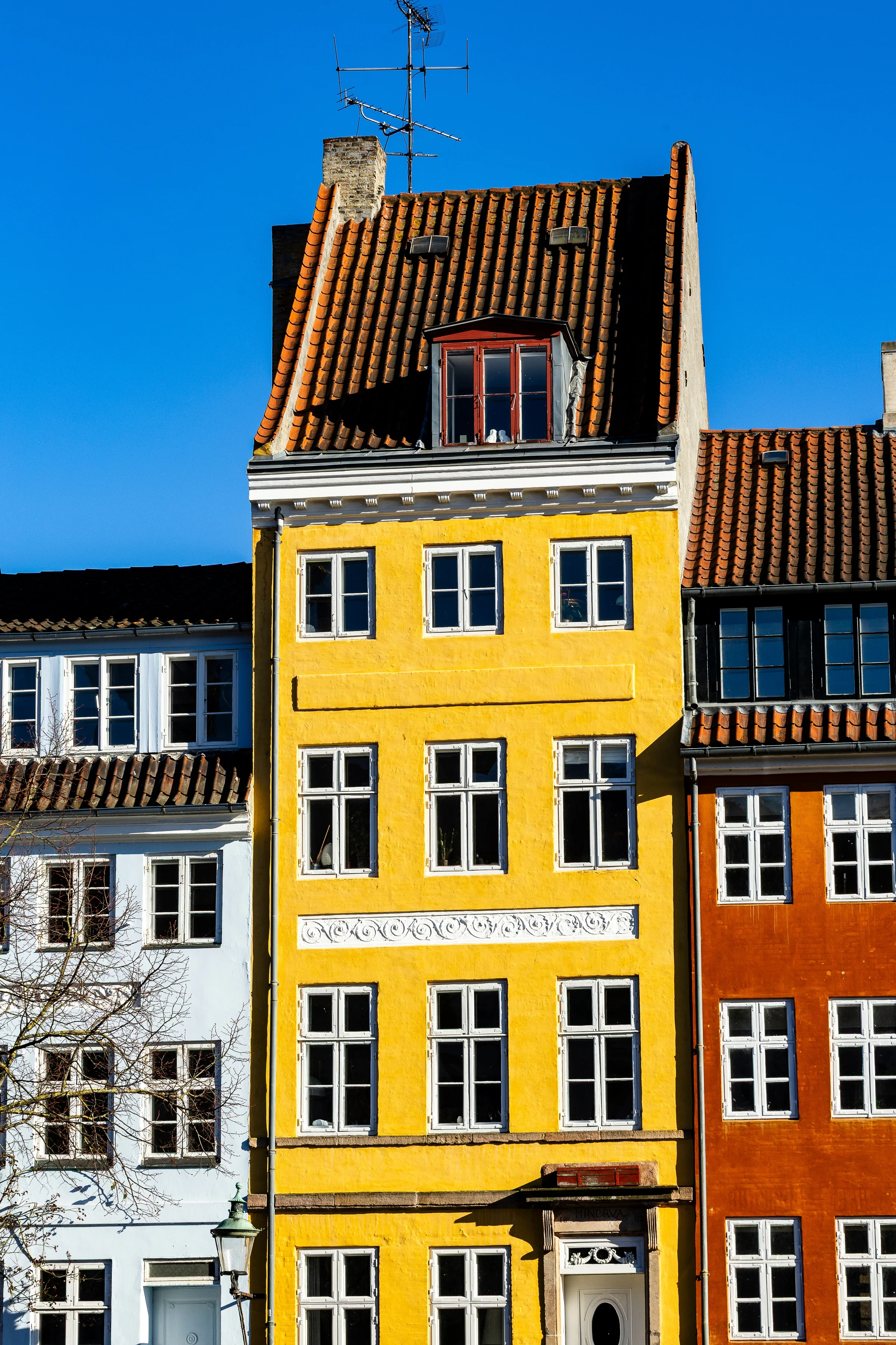 Fasad rumah kuning dan jingga di tepi kanal Nyhavn Copenhagen berlatar langit biru