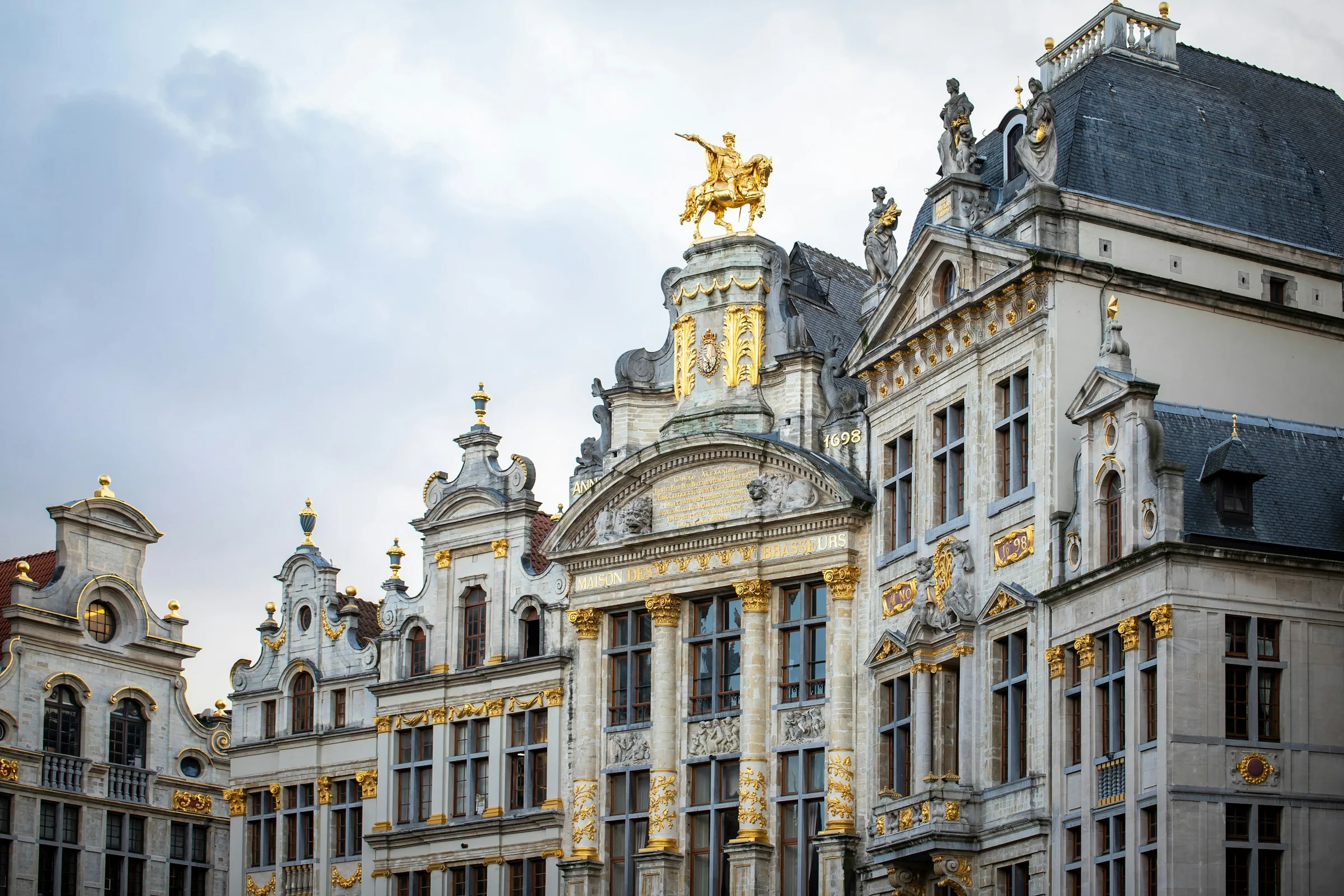 Gedung-gedung guild berhias emas di Grand Place Brussels dengan langit putih pucat.