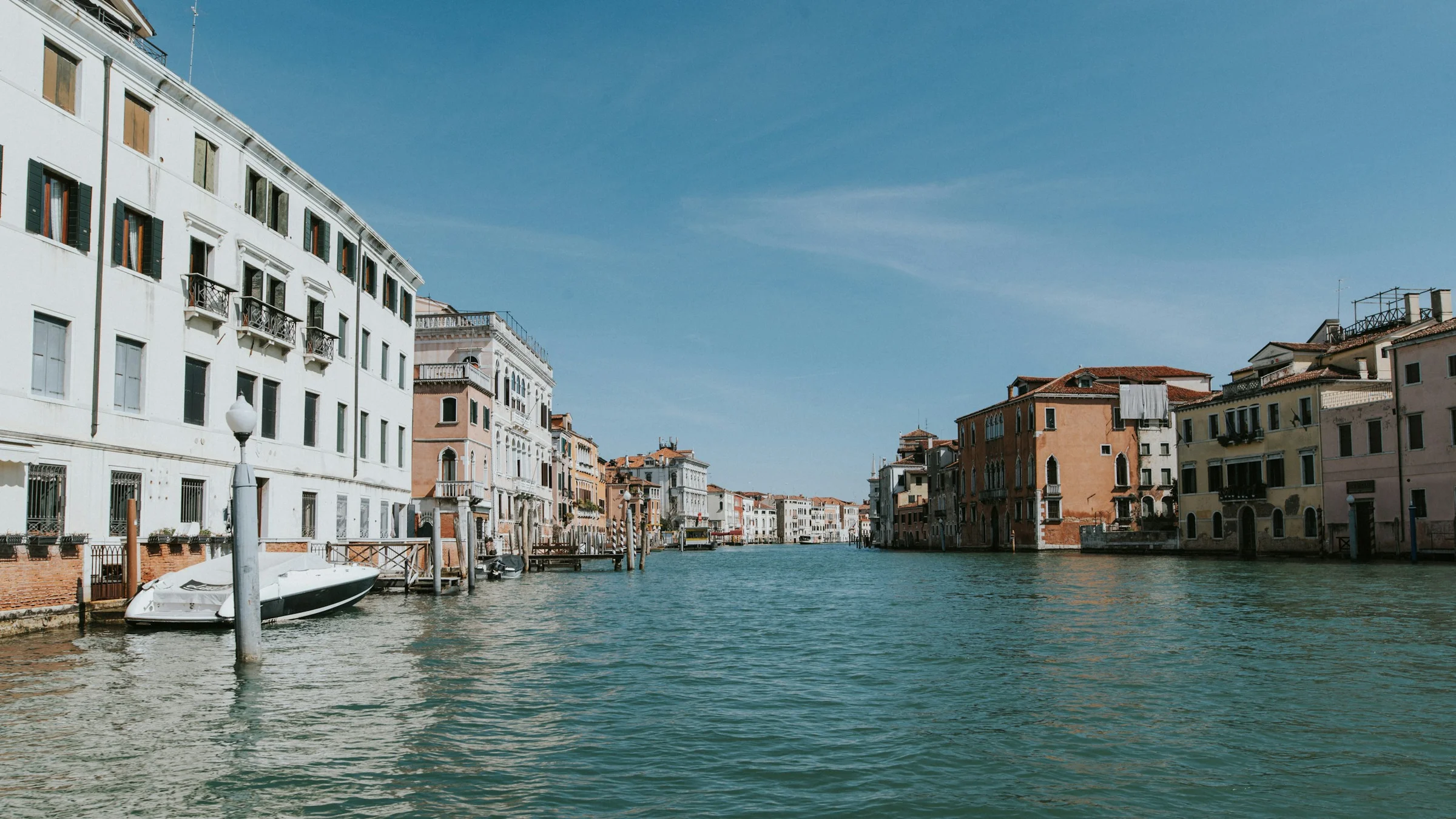 Kanal Venice dengan perahu di bawah langit biru berawan.