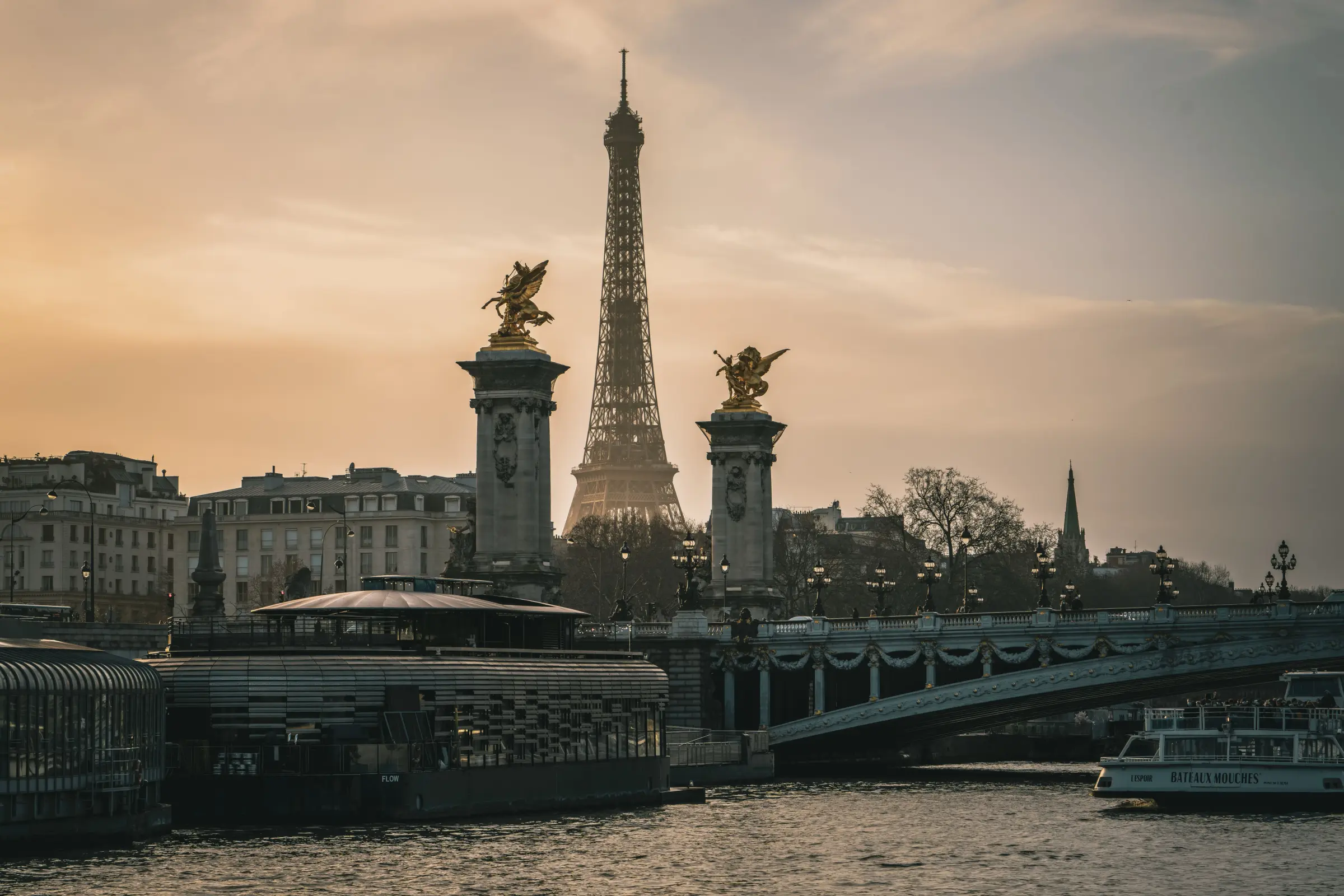 Menara Eiffel dan patung emas Pont Alexandre III bermandi cahaya senja di tepi Sungai Seine