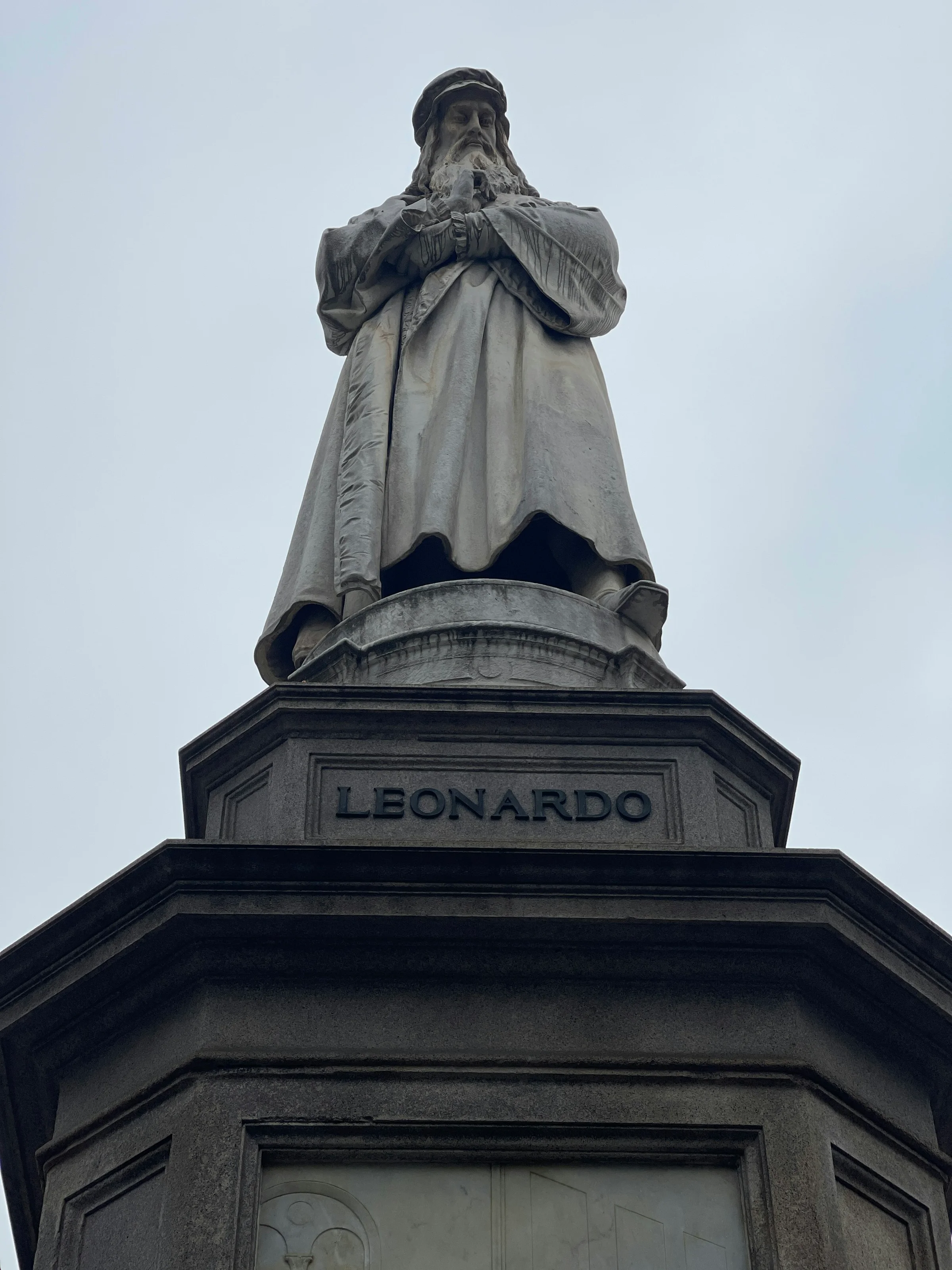 Patung Leonardo da Vinci di Piazza della Scala Milan dengan latar langit pucat.