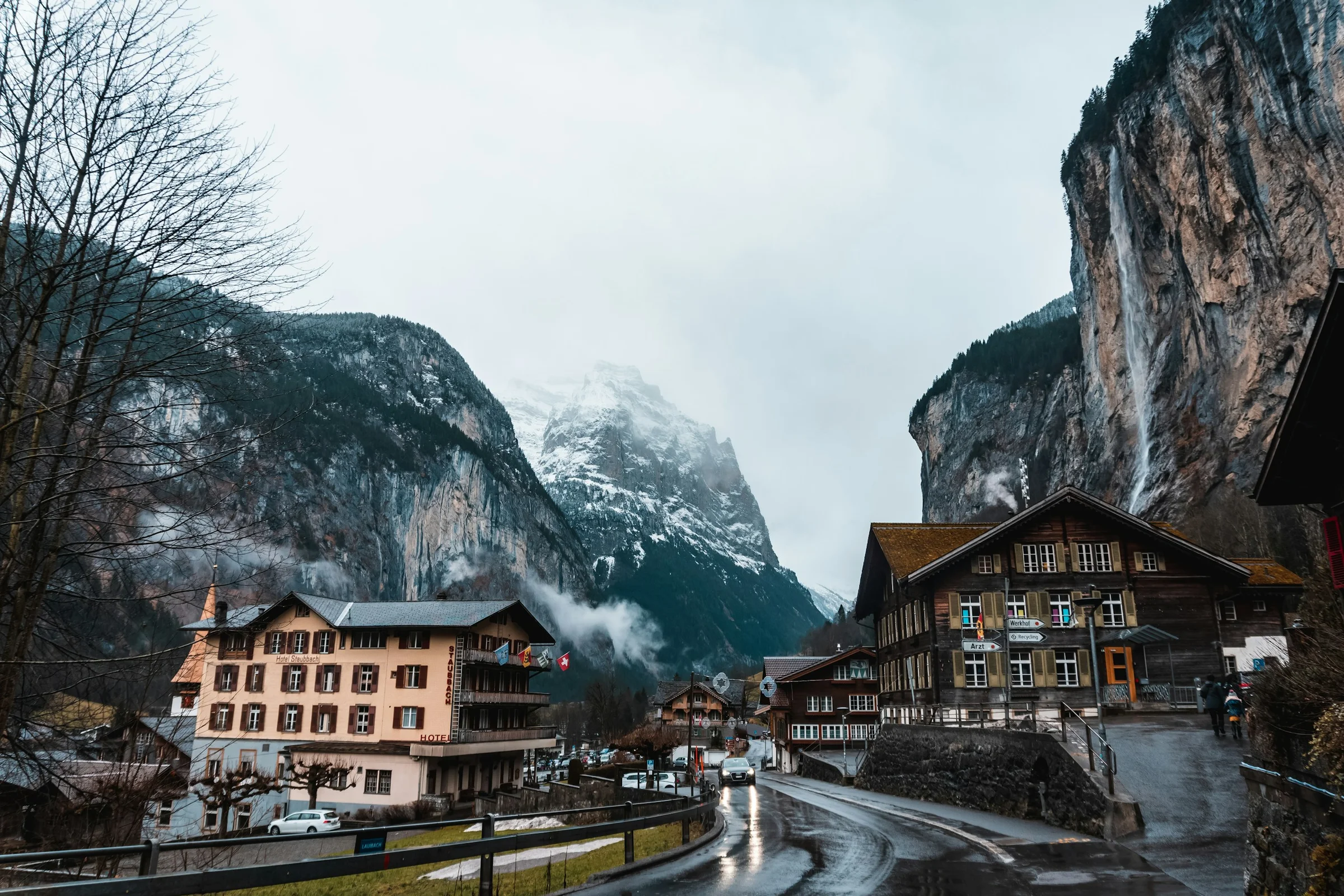 Desa Lauterbrunnen dengan tebing tinggi dan air terjun, jalan basah, dan puncak bersalju di lembah Swiss.