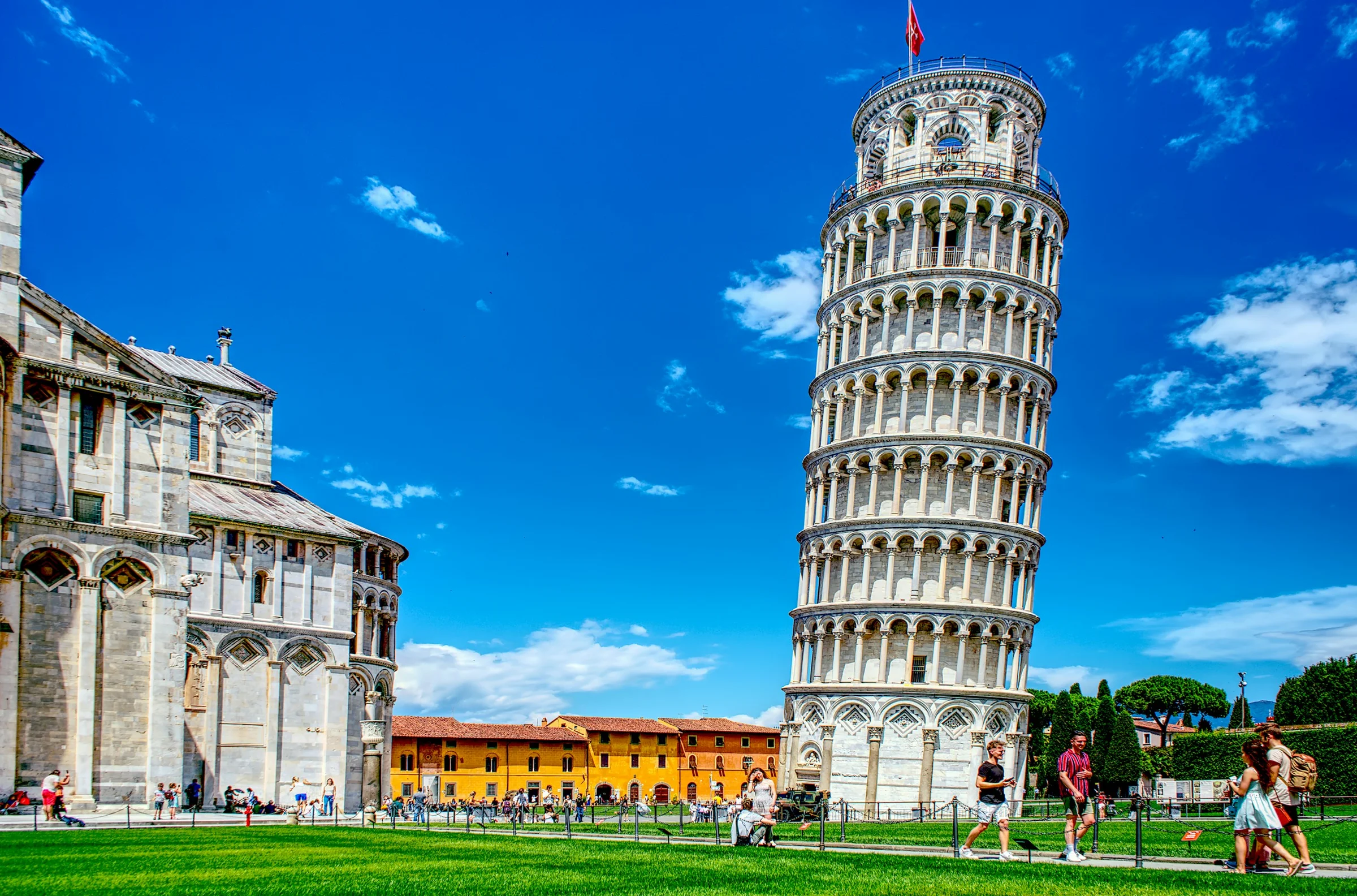 Menara Miring dan Katedral Pisa dengan rumput hijau dan langit biru berawan, Italia.