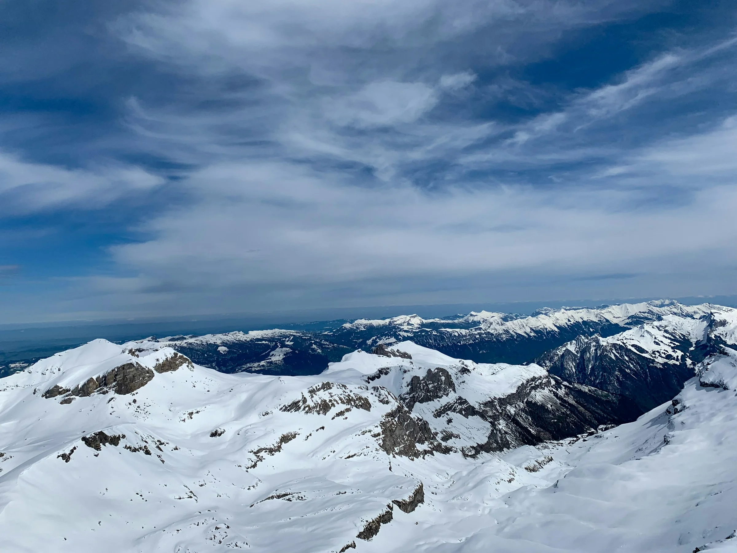 Punggungan Alpen bersalju di bawah langit biru bergaris awan, kawasan Jungfrau Swiss.