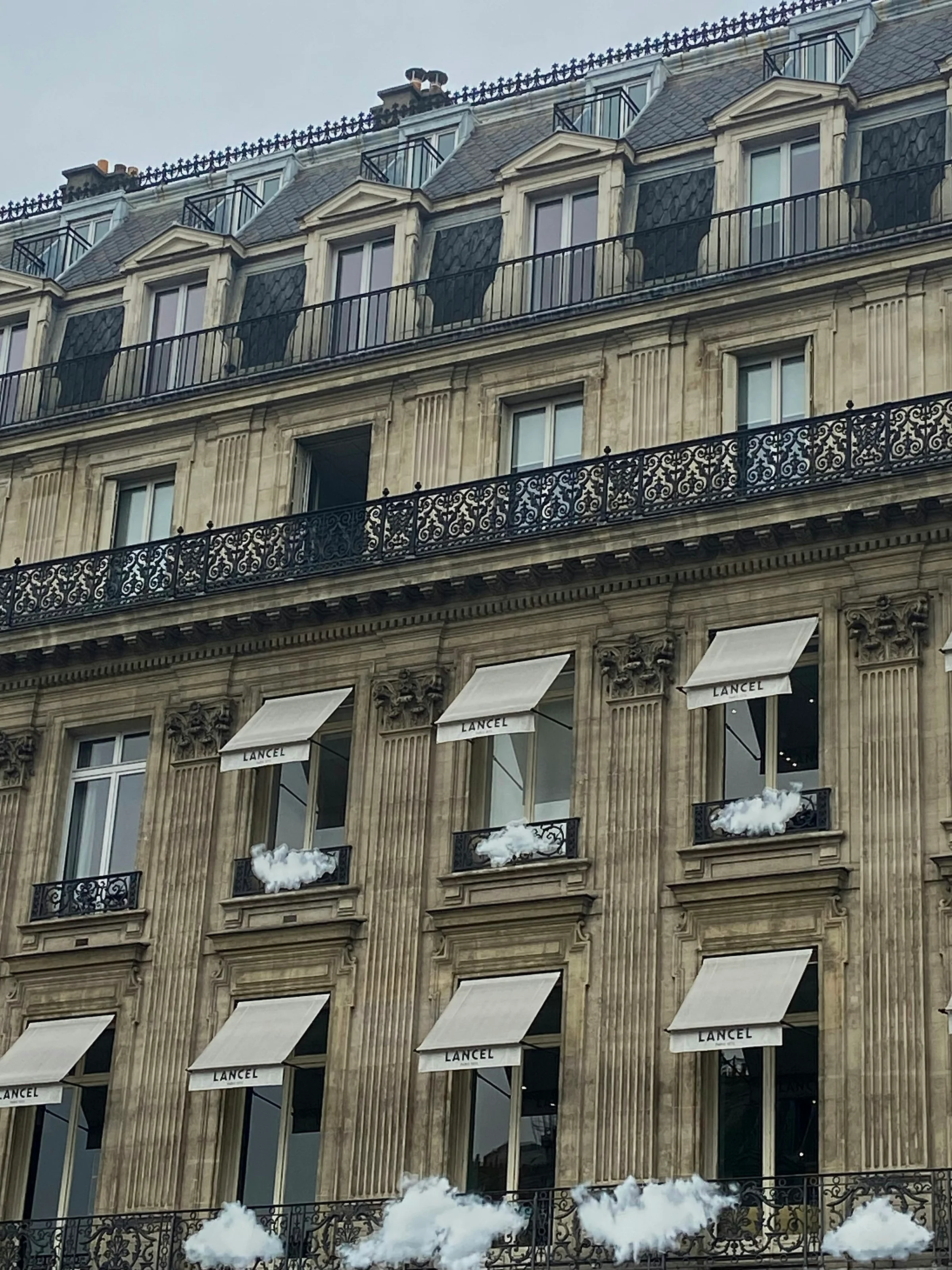 Fasad bangunan bergaya Haussmann di Paris dengan balkon besi tempa dan tenda jendela.
