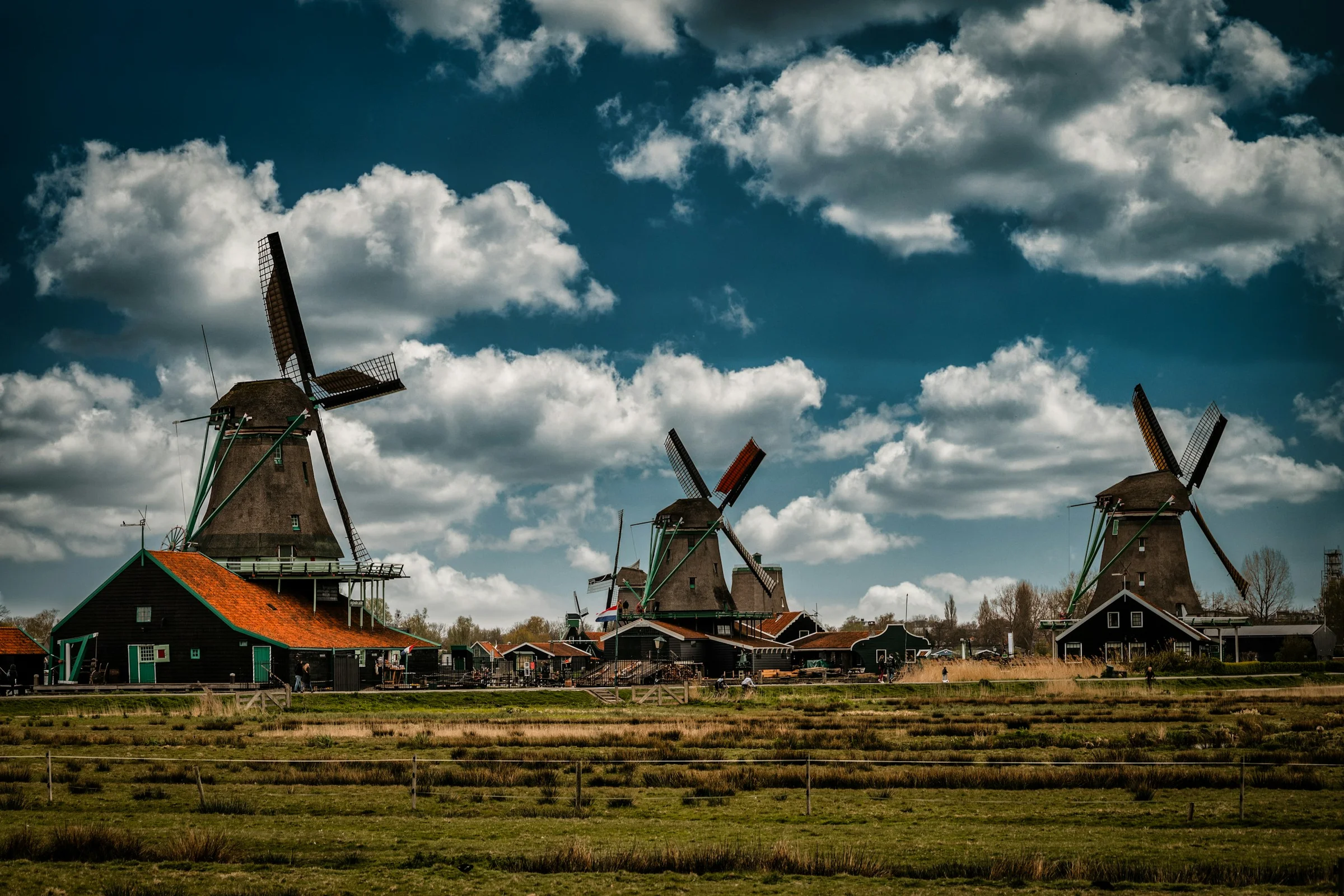 Kincir angin Zaanse Schans dengan rumput kecokelatan dan awan dramatis, Belanda.