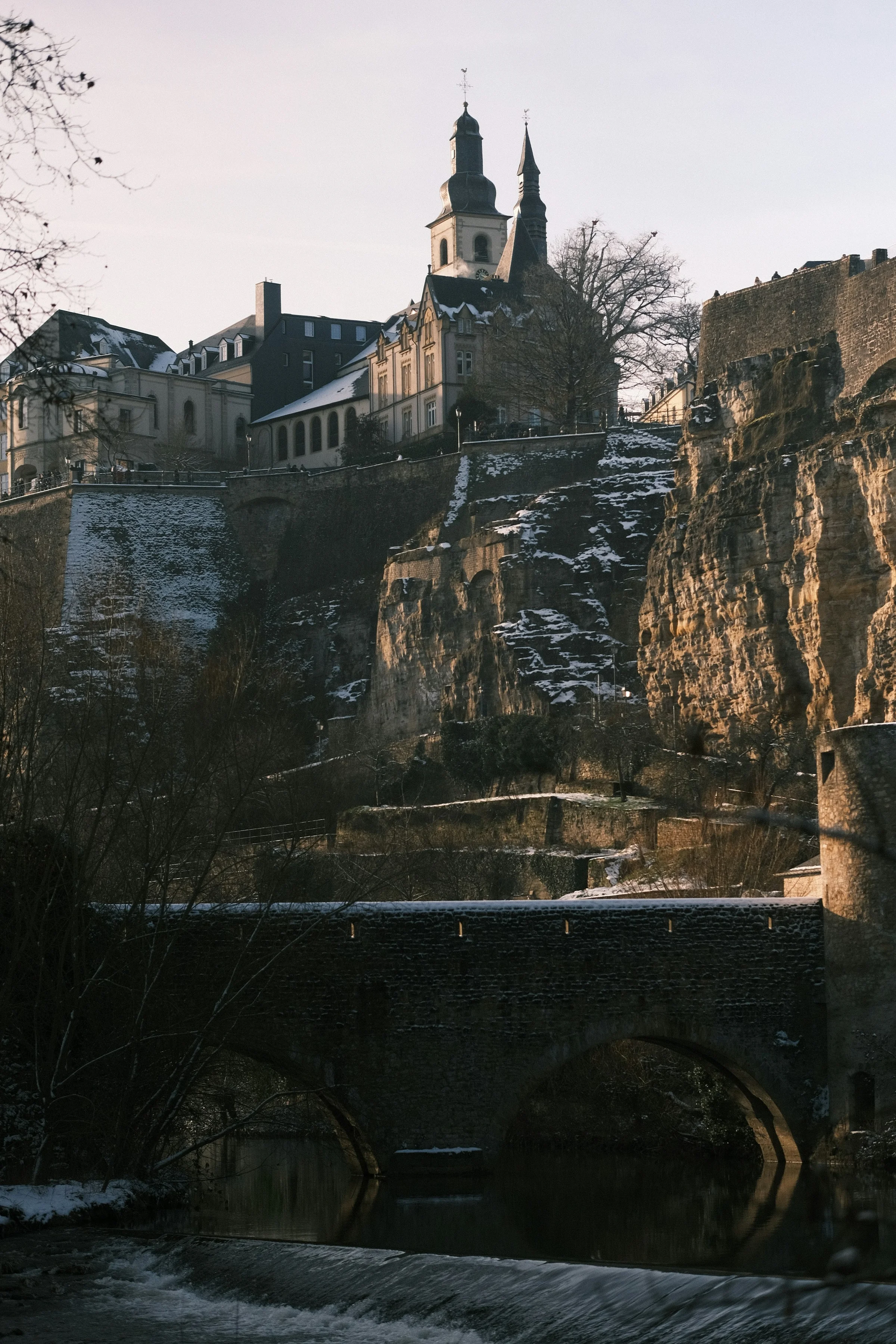 Tebing batu dan jembatan kota tua Luxembourg dengan menara gereja di atasnya.