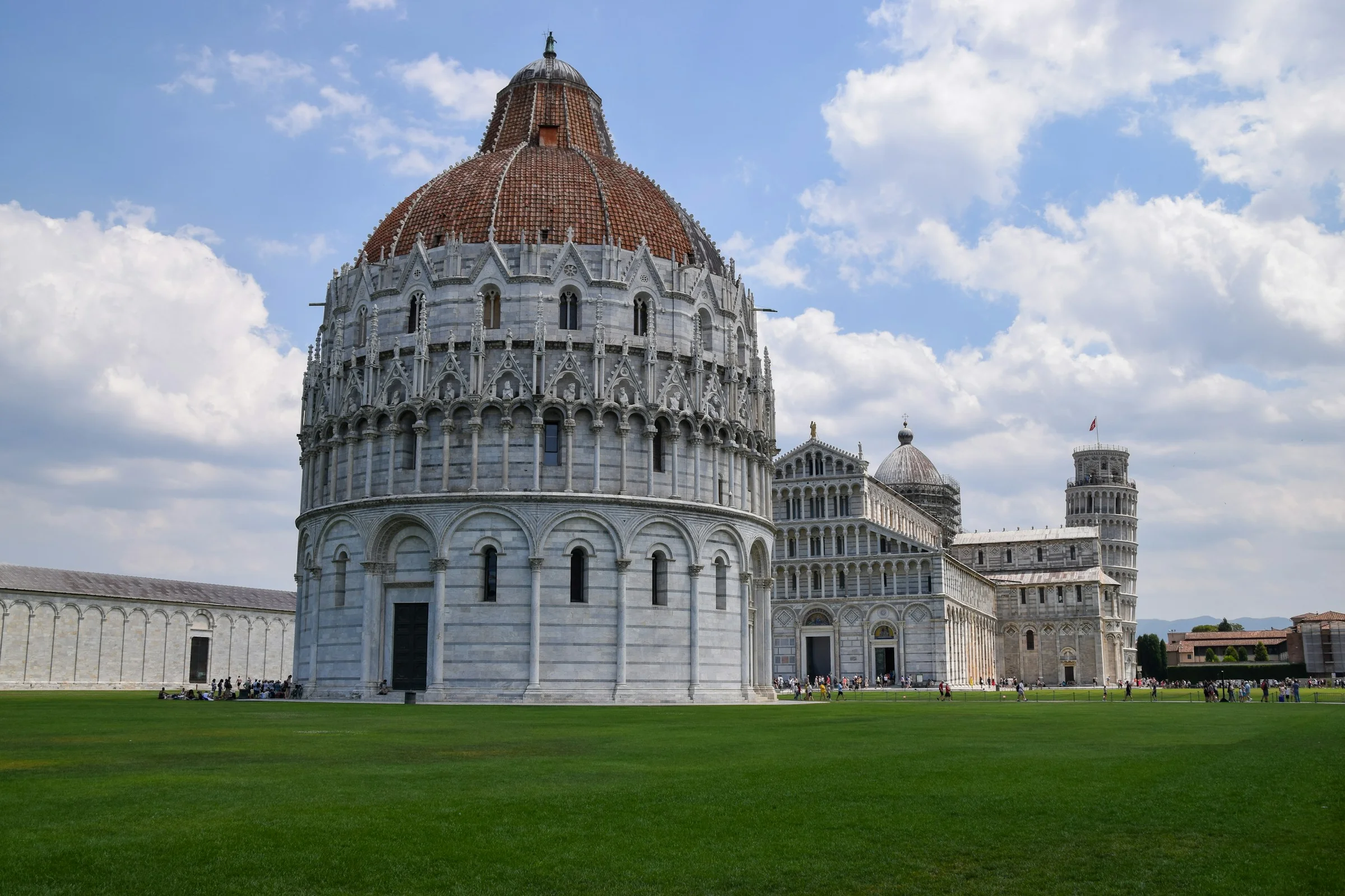 Baptistery Pisa dengan Menara Miring di latar belakang dan langit biru berawan.