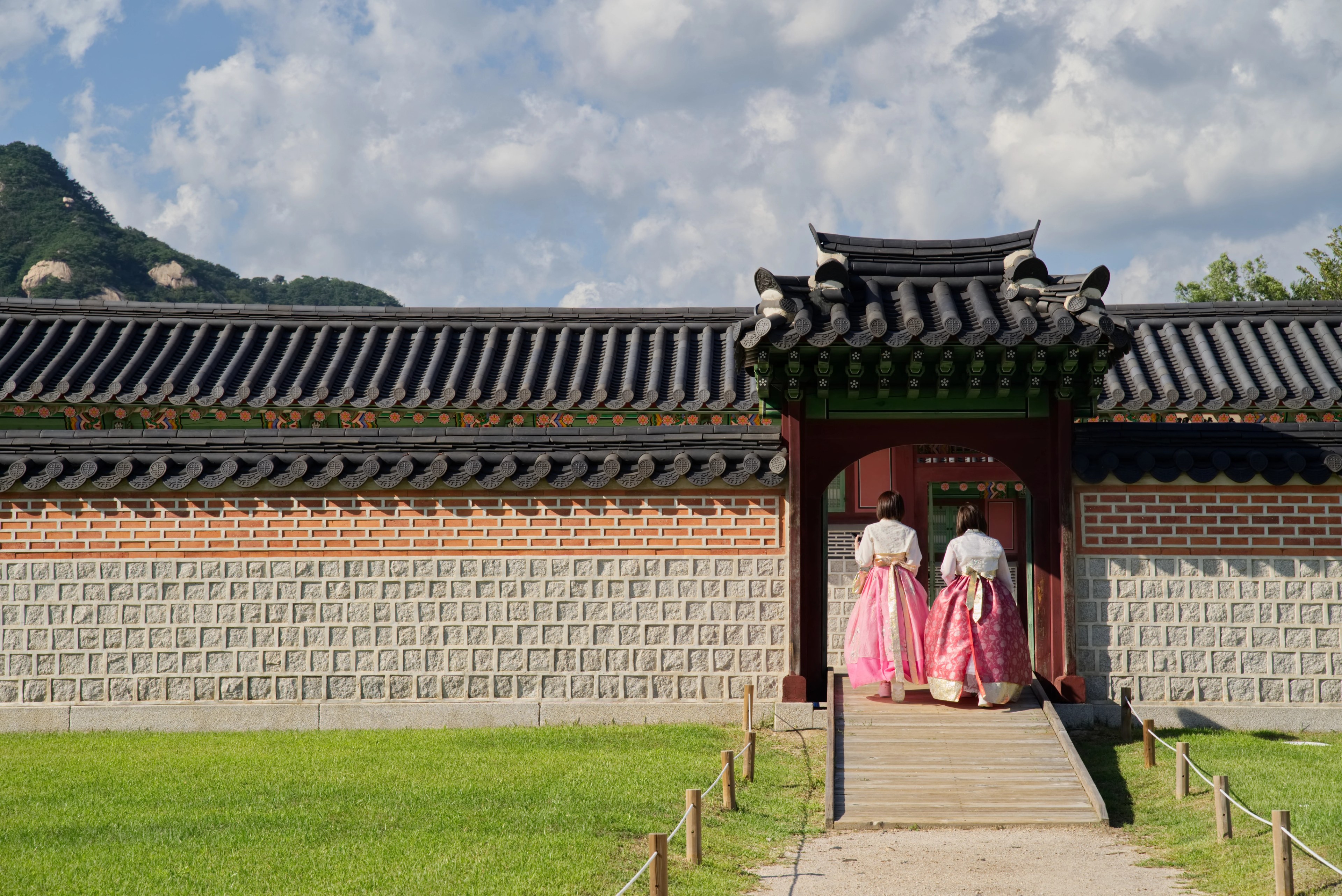 Gerbang Gyeongbokgung di Seoul saat musim semi, pengunjung berhanbok di halaman dan pohon berbunga di sisi kiri, Korea Selatan