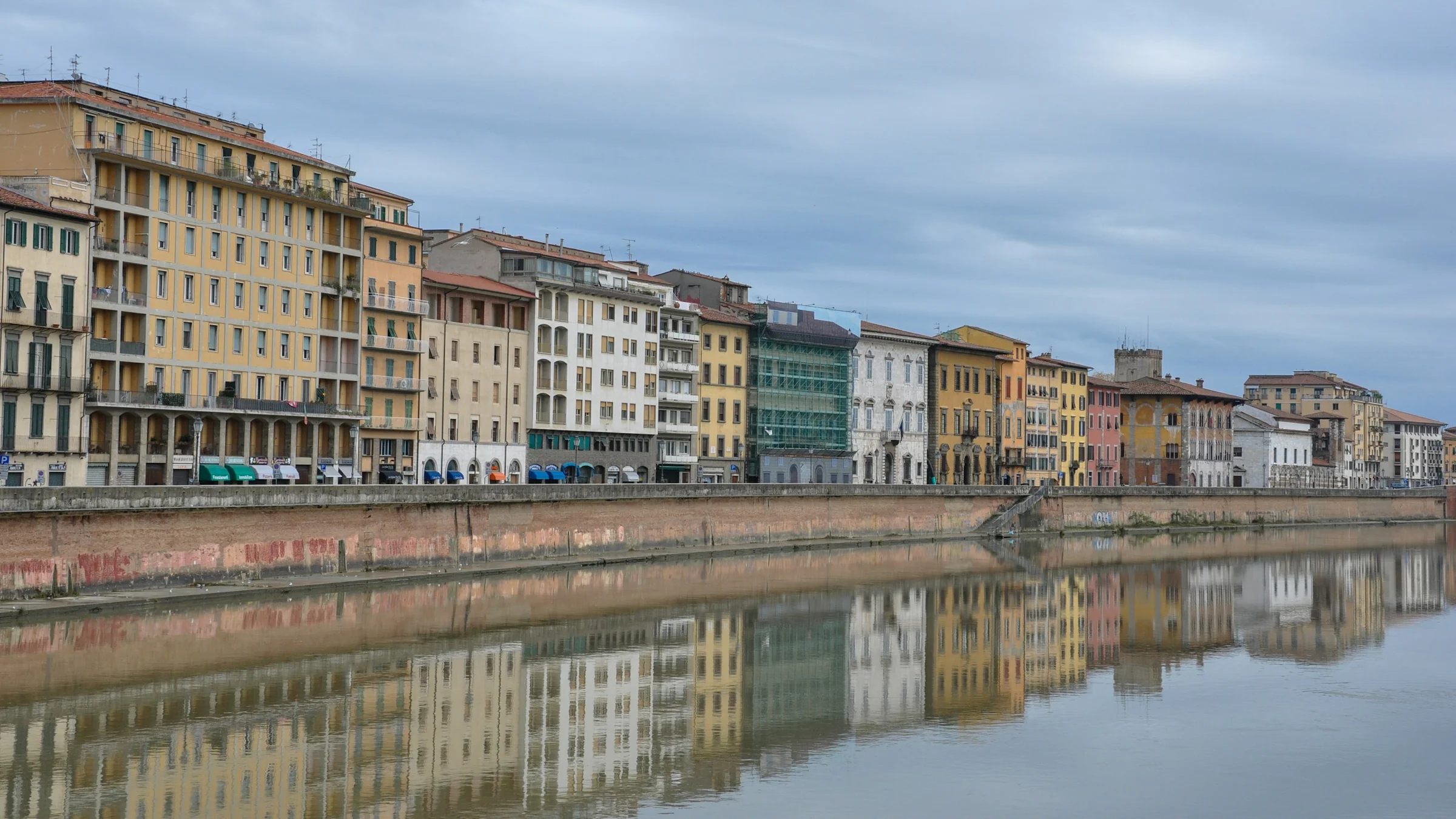 Gedung-gedung tepi Sungai Arno di Pisa dengan pantulan di air.