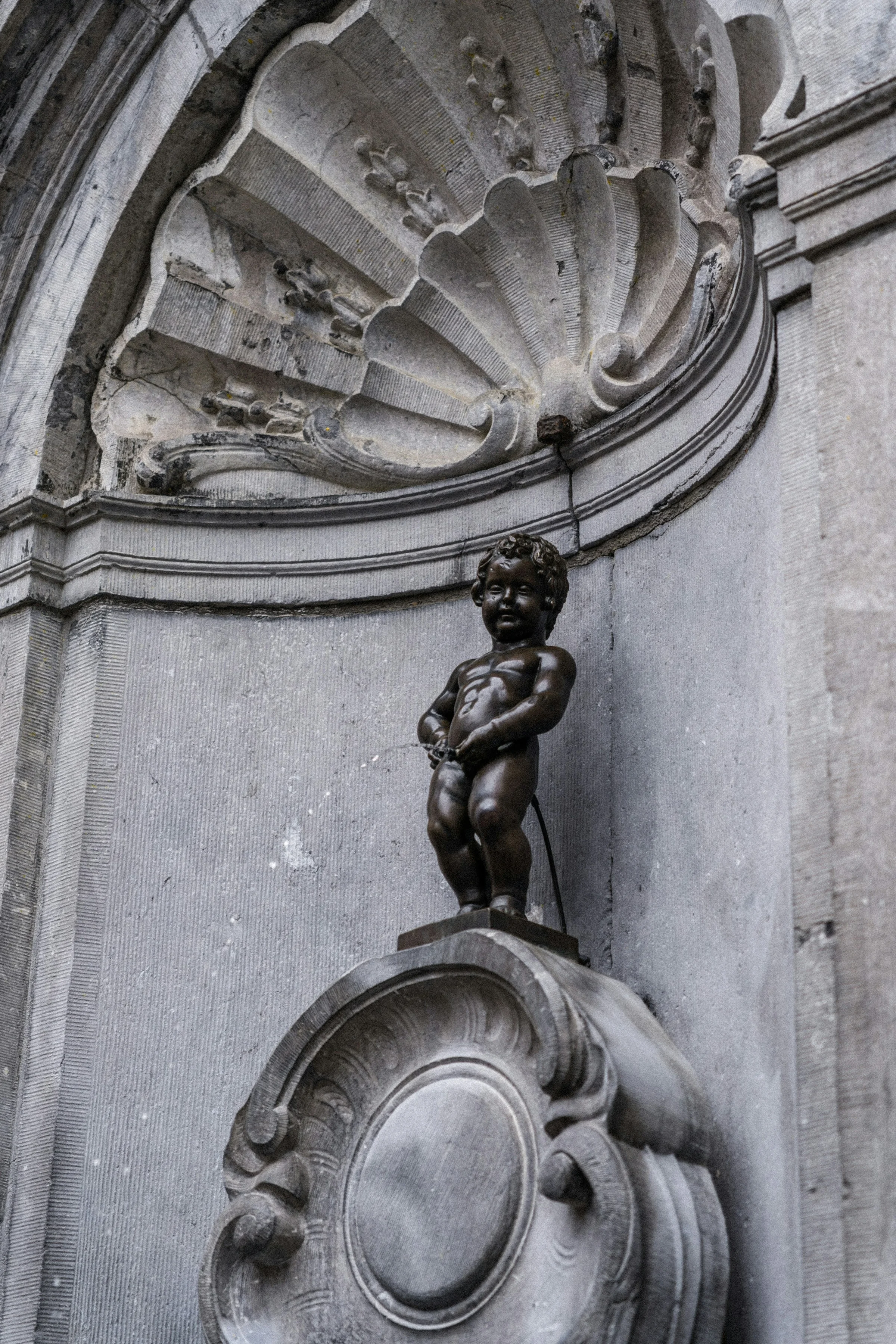 Patung Manneken Pis di Brussels dengan latar abu-abu polos.