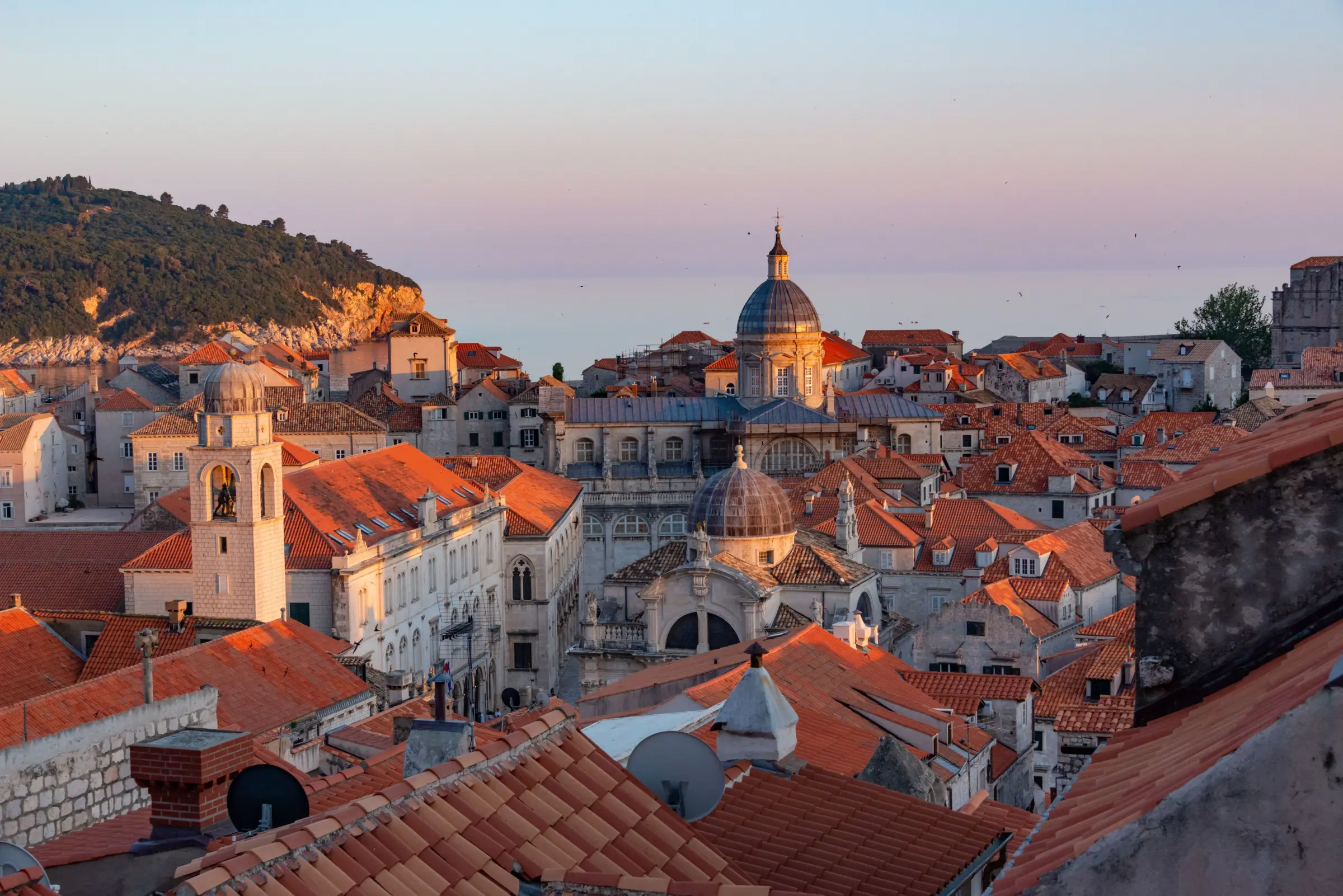 Matahari terbenam di atas atap genteng terakota Kota Tua Dubrovnik, Kroasia, dengan kubah katedral menghadap Laut Adriatik.
