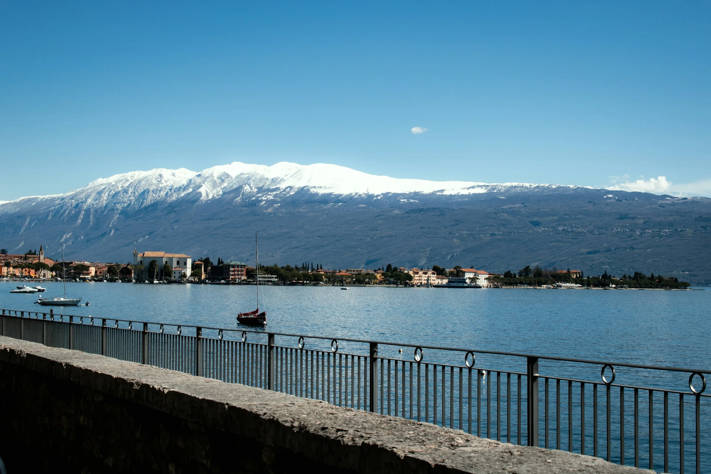 Promenade tepi Danau Garda dengan puncak Monte Baldo yang bersalju di kejauhan.