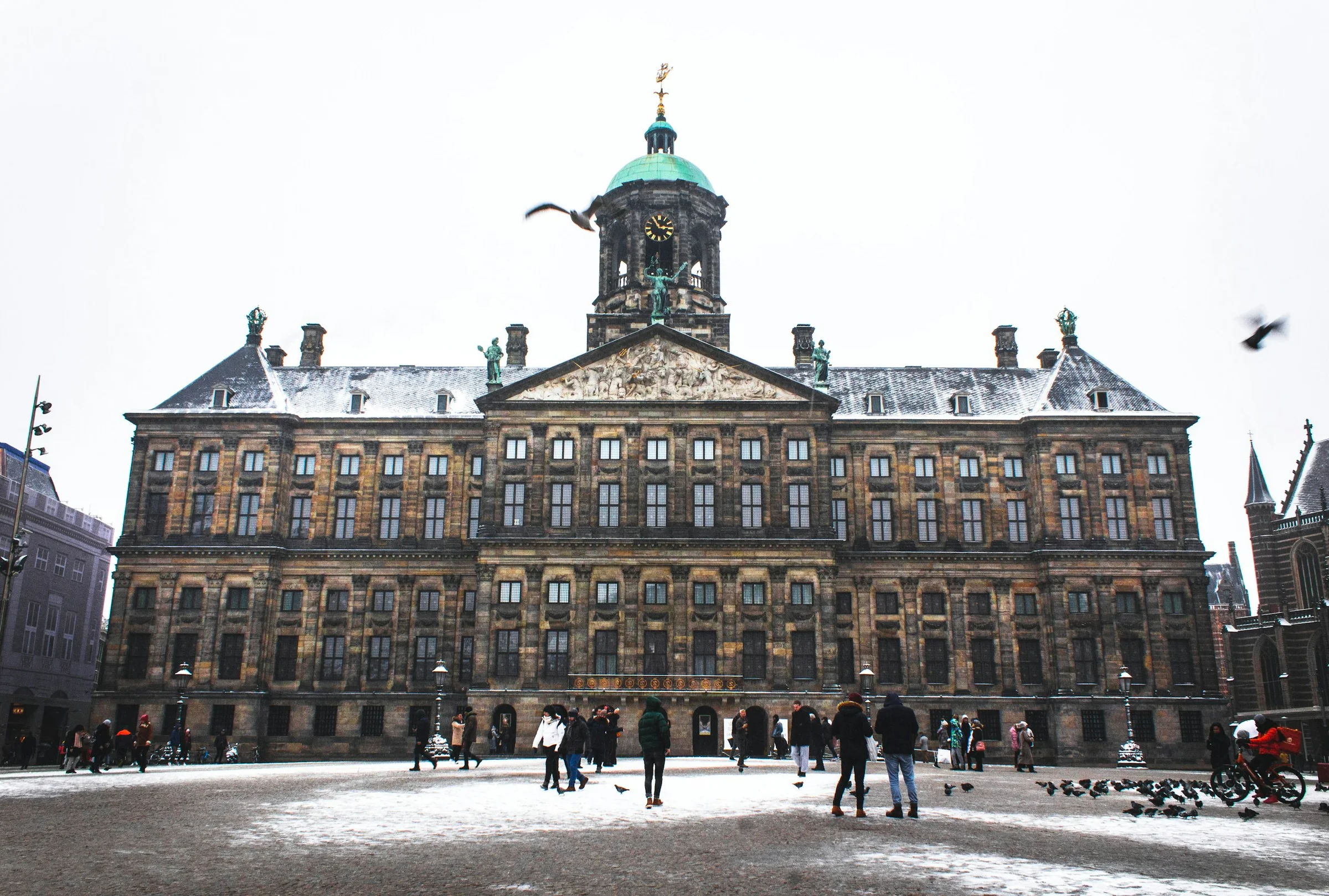 Royal Palace di Dam Square Amsterdam tertutup salju tipis dengan burung-burung beterbangan.
