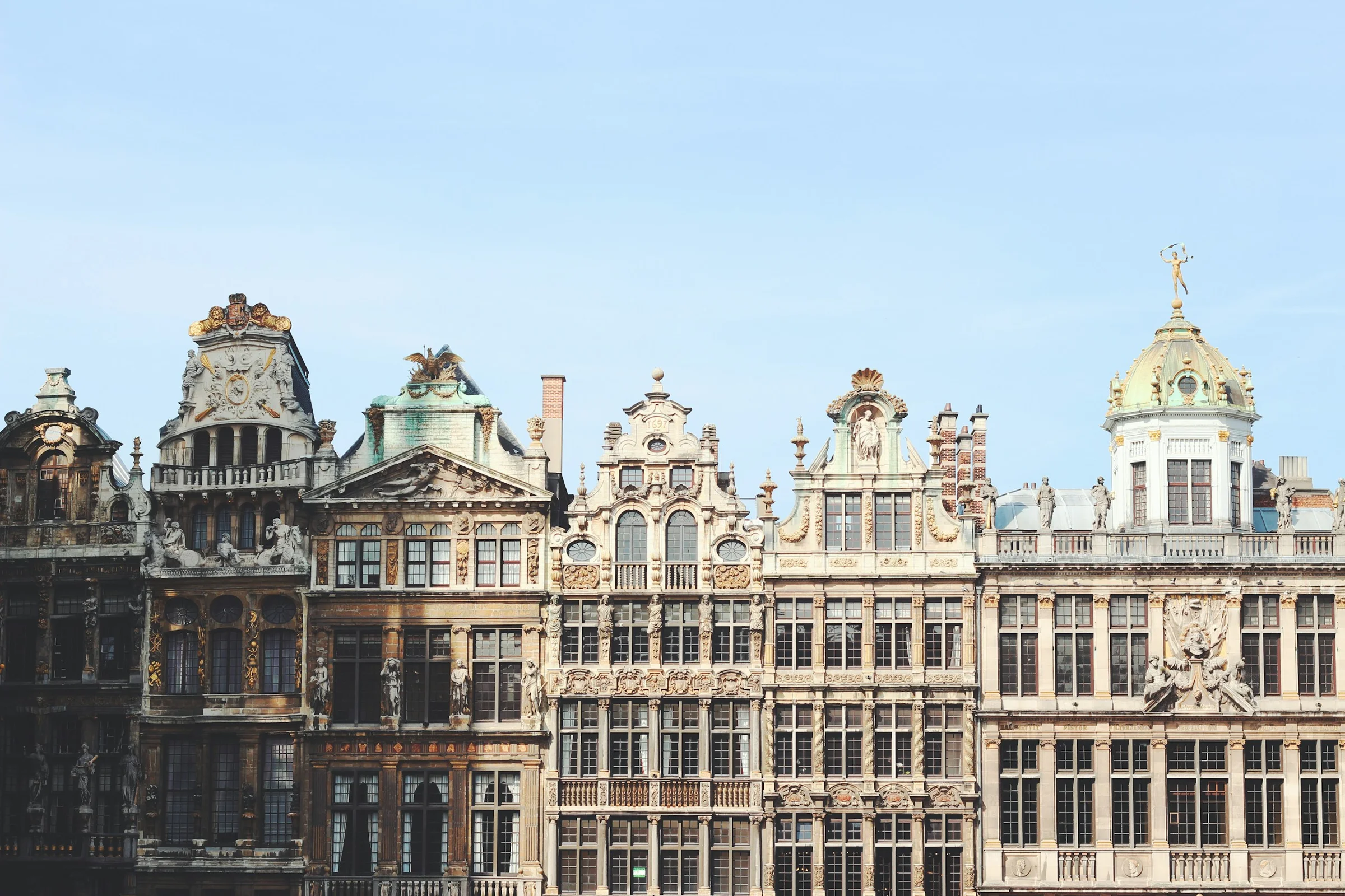 Deretan gedung guild di Grand Place Brussels dengan langit biru pucat.