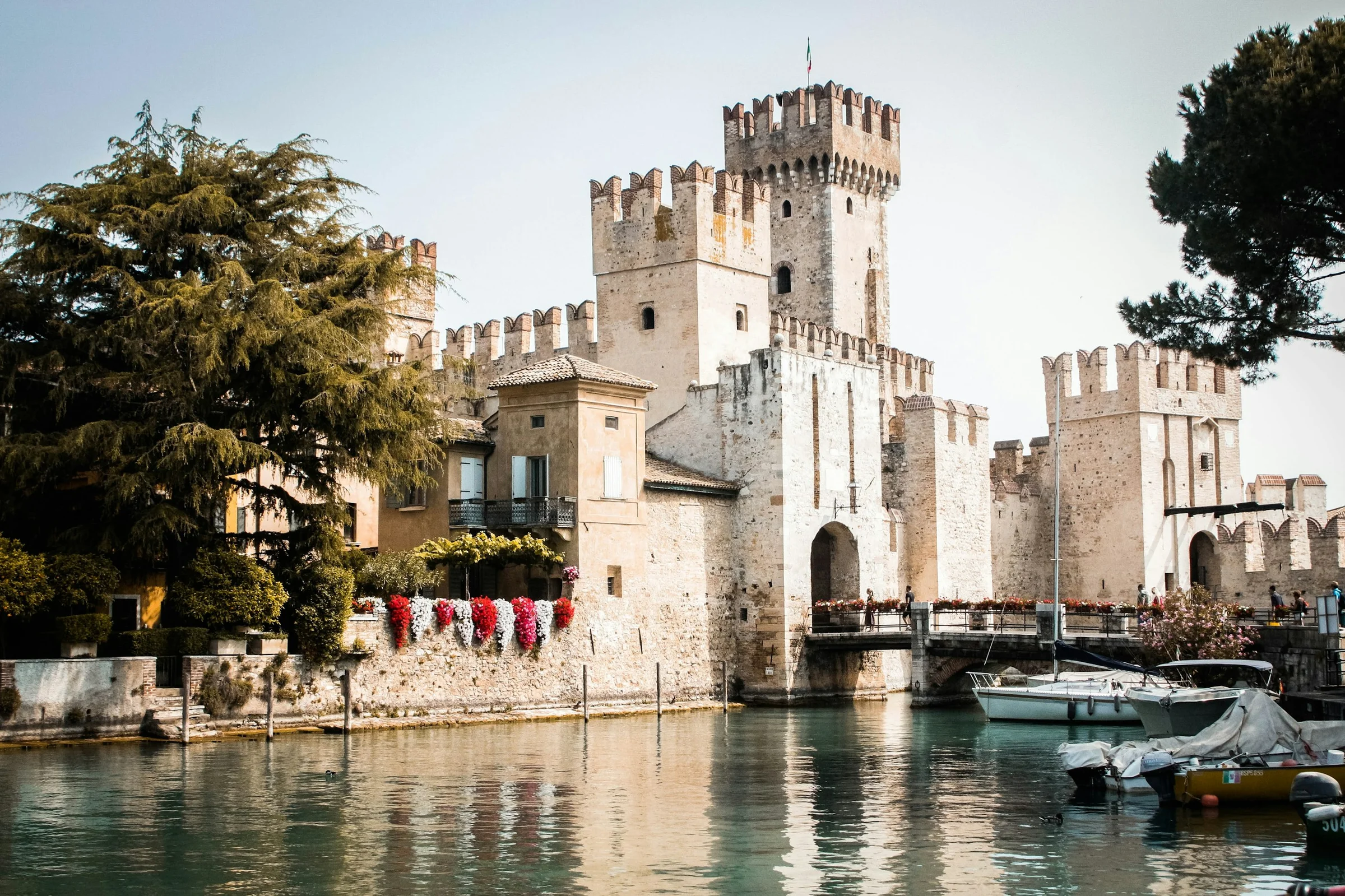 Kastil Scaligero di Sirmione dengan pohon pinus dan perahu di Danau Garda, Italia.