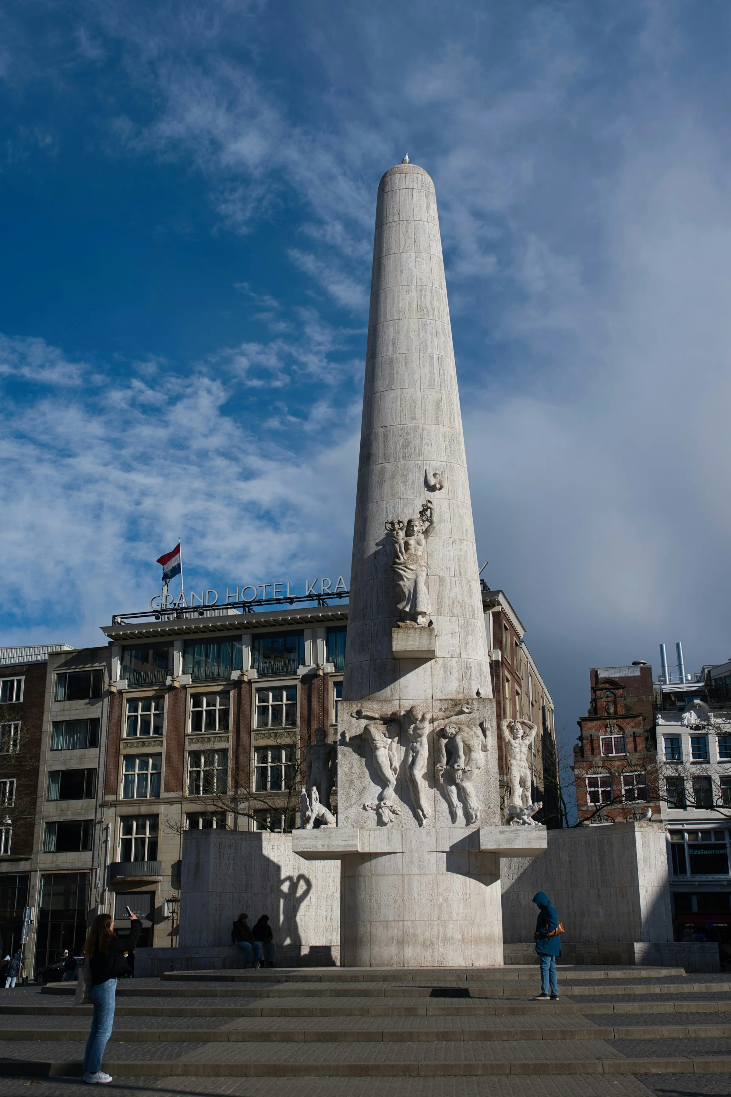 Monumen Nasional di Dam Square Amsterdam dengan langit biru dan awan tipis.