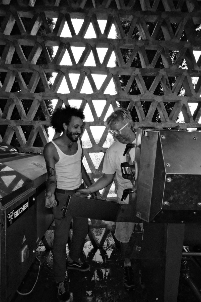 Two of the collective working the harvest machine under a brick lattice