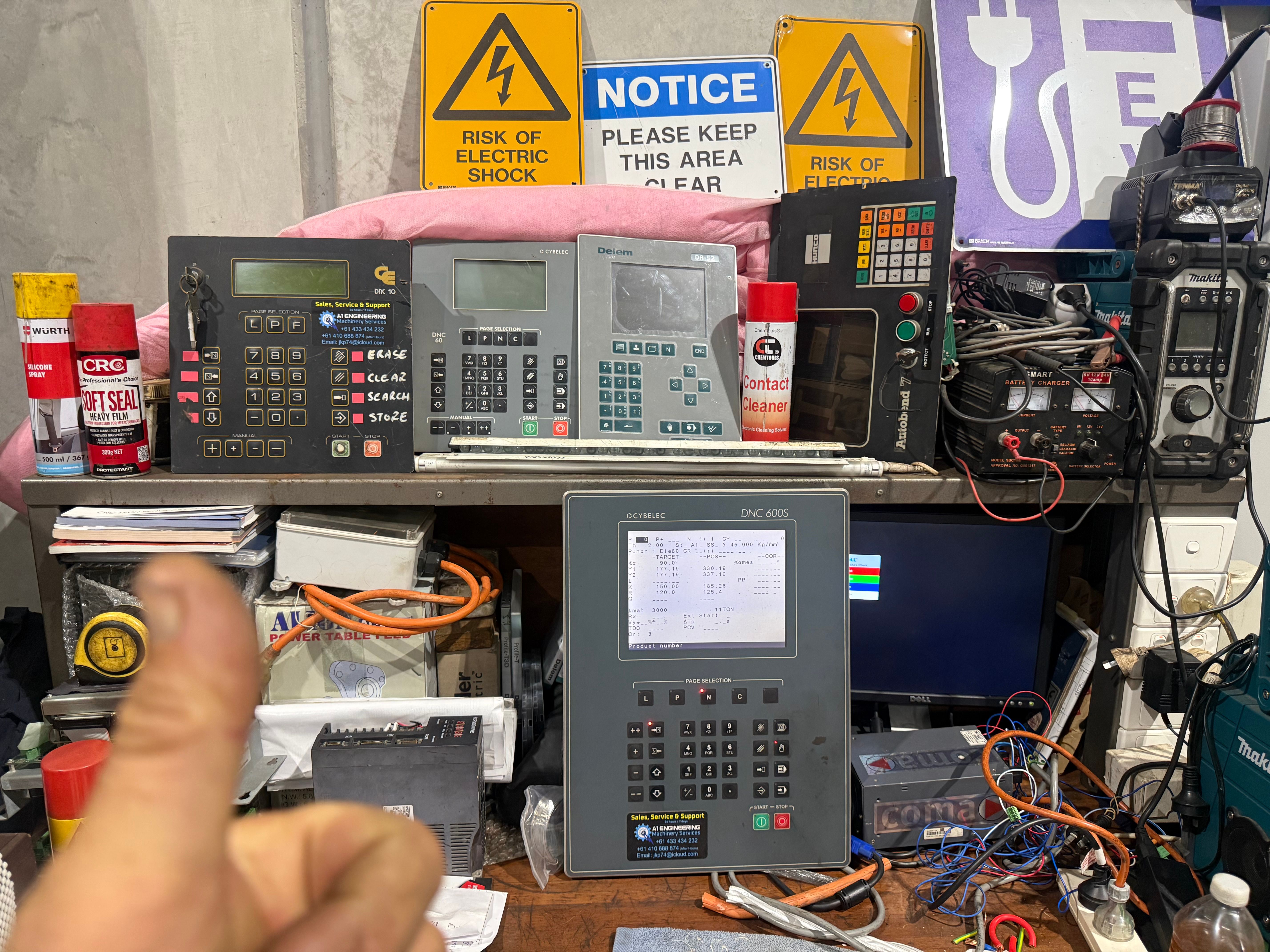 A workshop bench holding several press brake controllers under test, including Cybelec DNC-series units and a Delem control head.