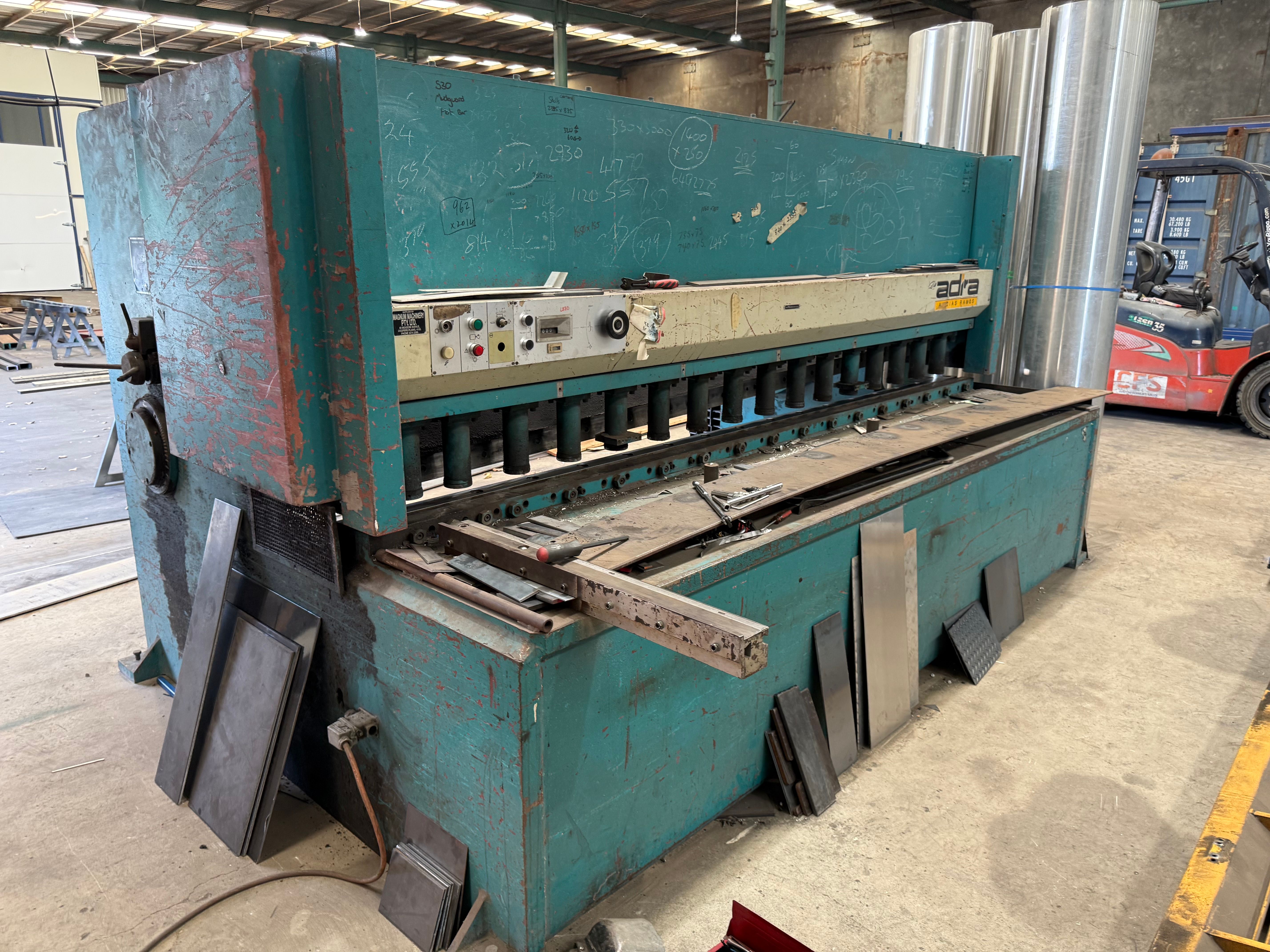 A teal Adira guillotine shear with its long blade bar and control panel visible on the workshop floor, newly fitted with blades.