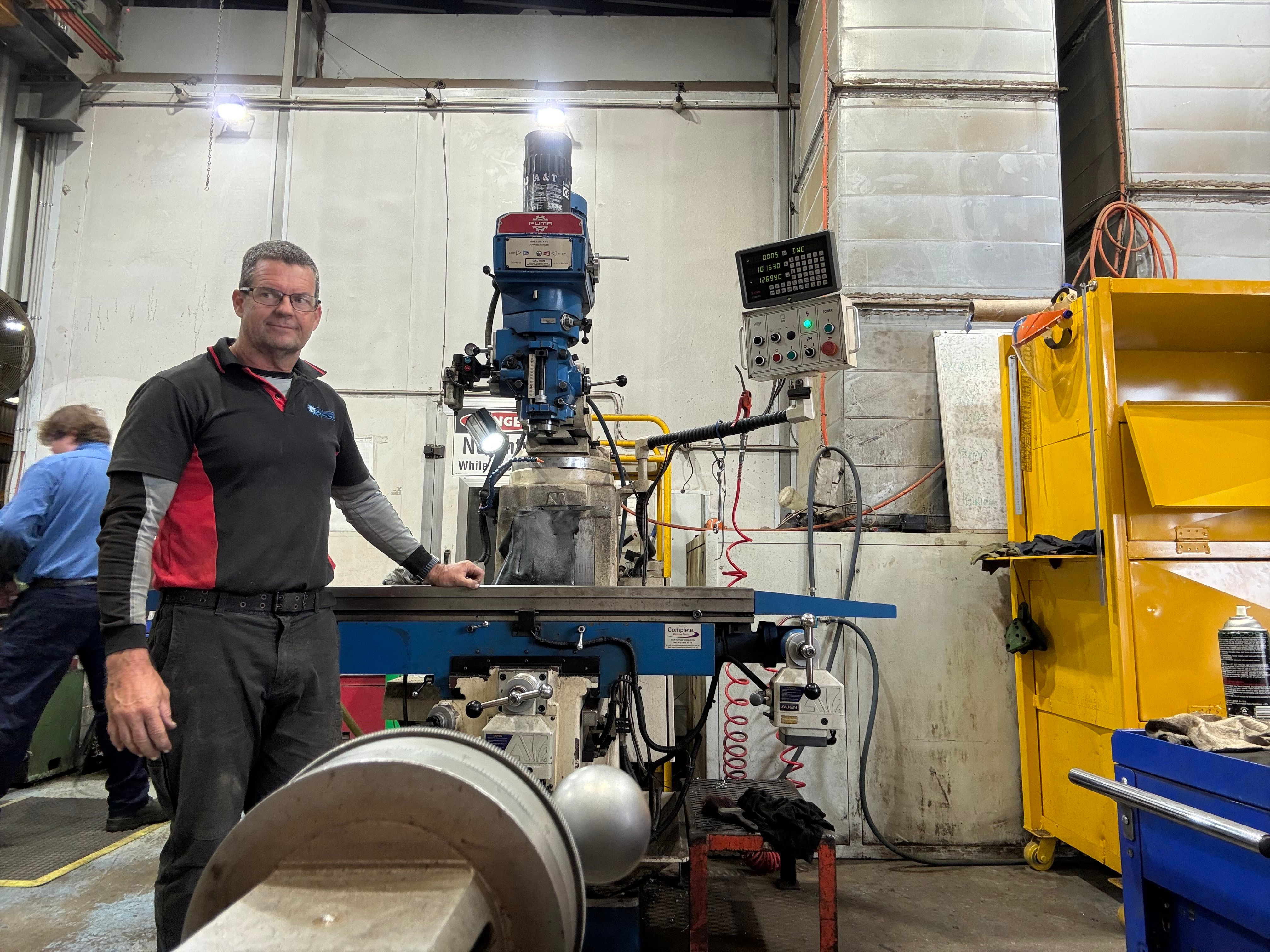 A blue turret milling machine fitted with a digital readout beside a technician in a workshop.