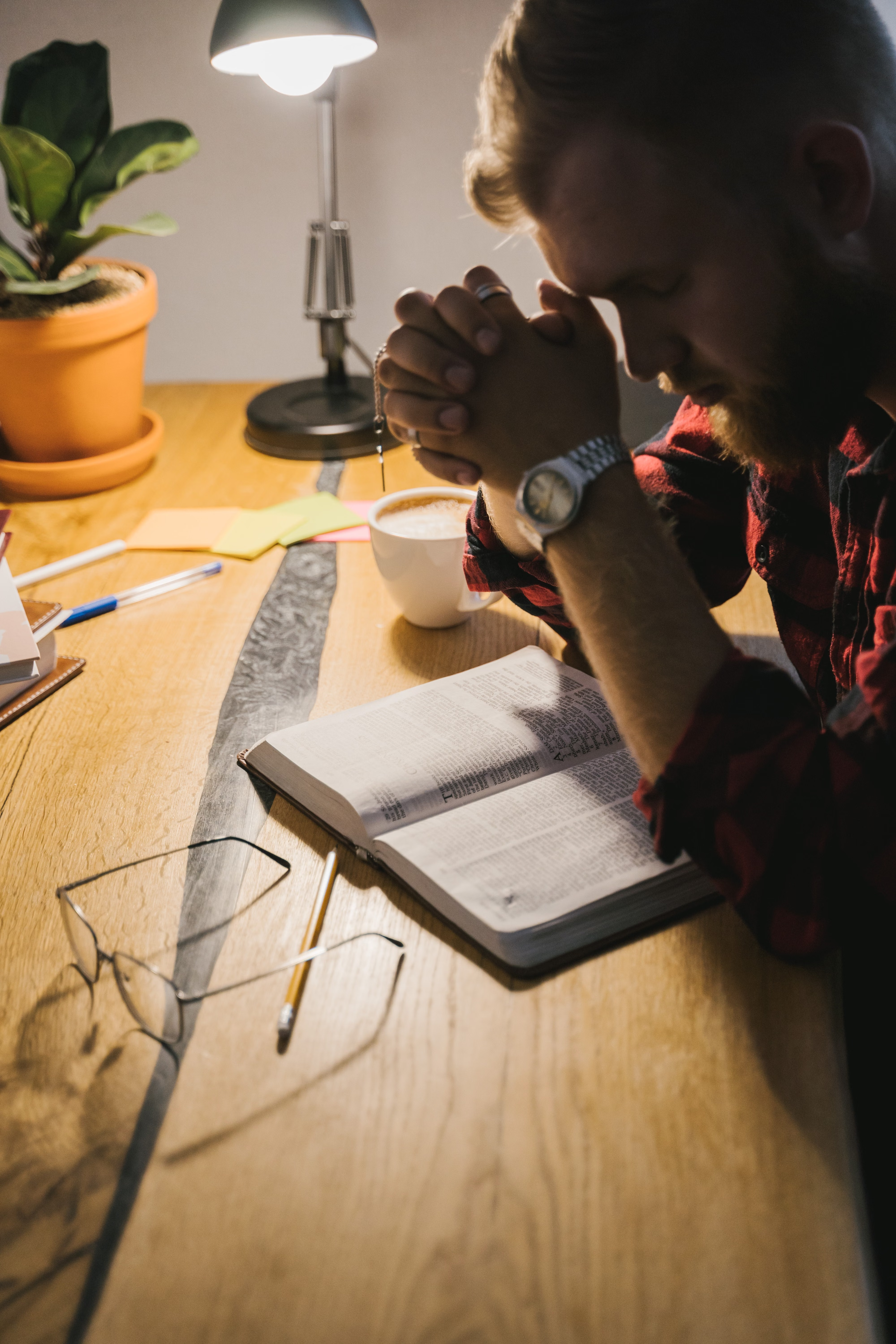 A man praying with an open Bible on a wooden table