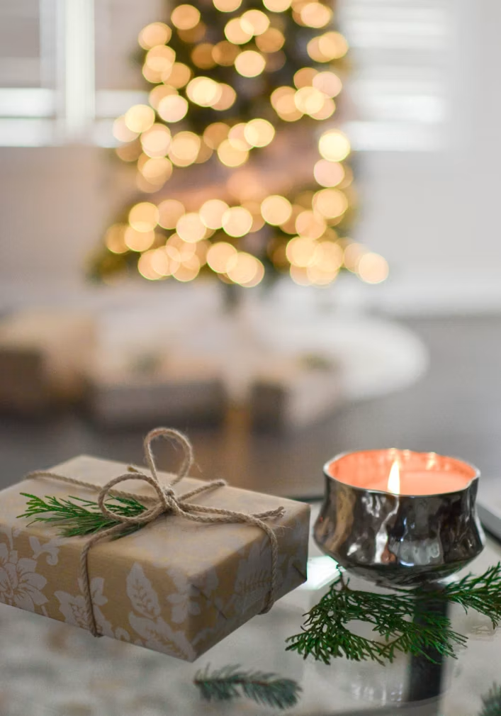 Alt text: A wrapped Christmas gift beside a candle and soft holiday lights
