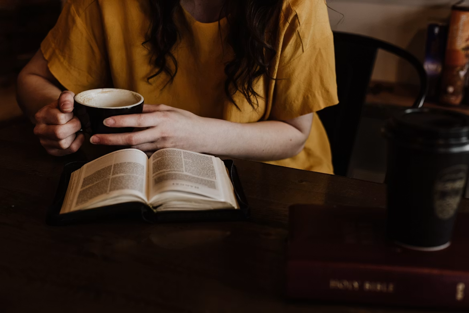 A woman holding coffee beside an open Bible