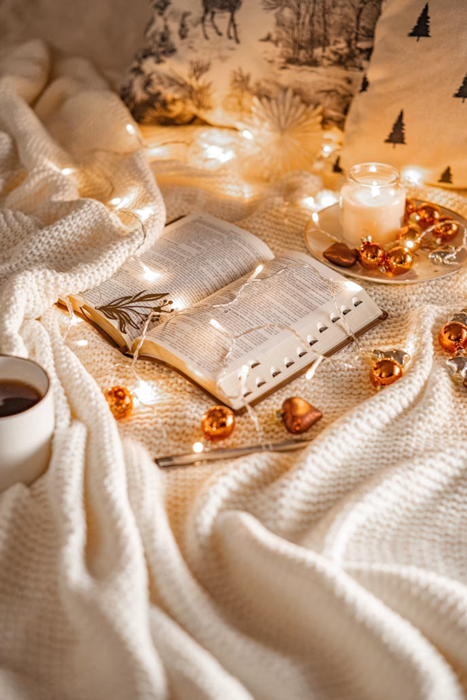An open Bible with candles and Christmas lights in a warm home setting