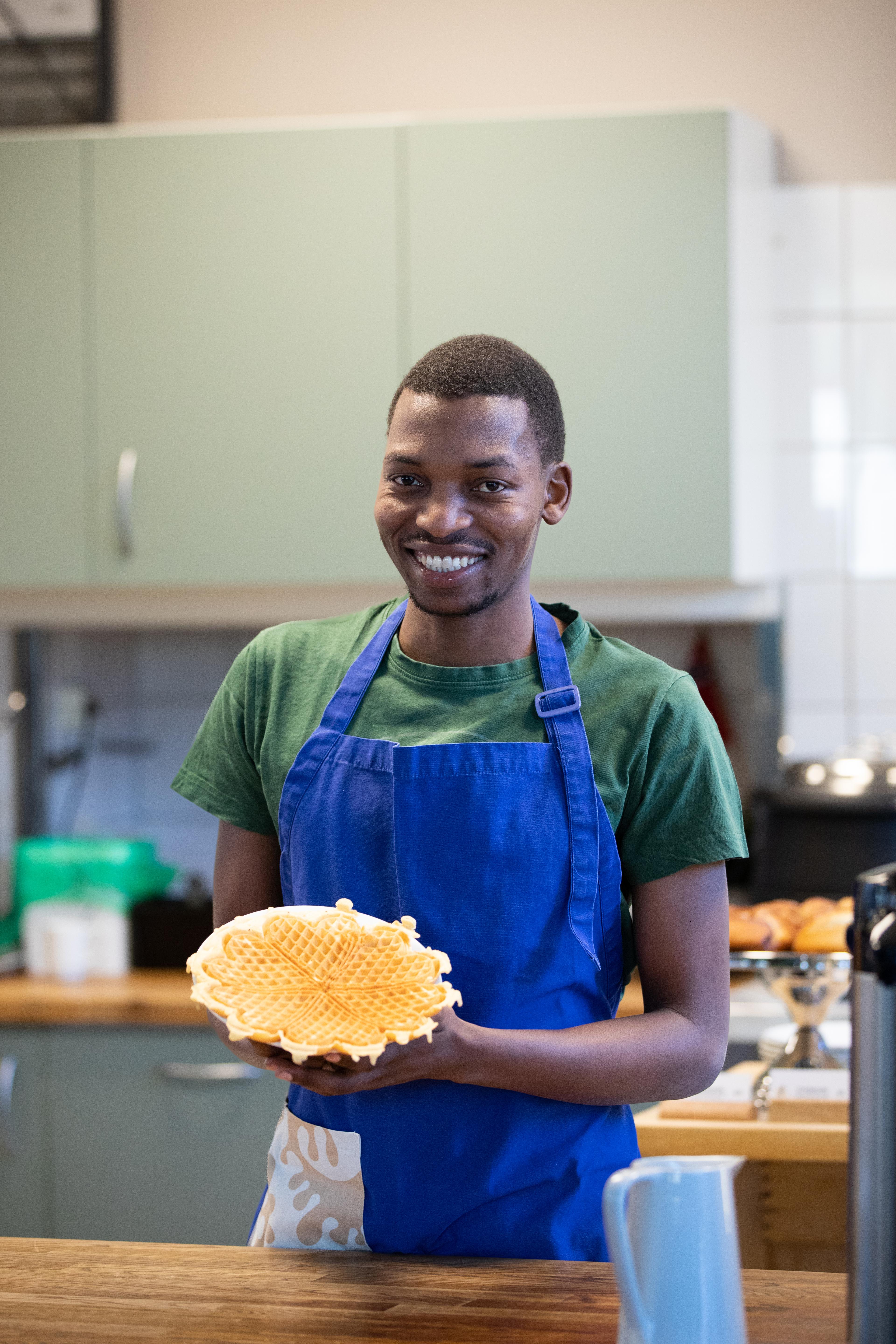 Ung mann med forkle, på et kjøkken, viser frem i vaffelplate.